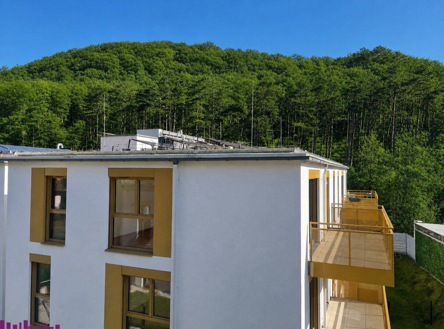 Moderne Gebäudefassade mit Balkonen und weitem Blick auf bewaldete Hügel.