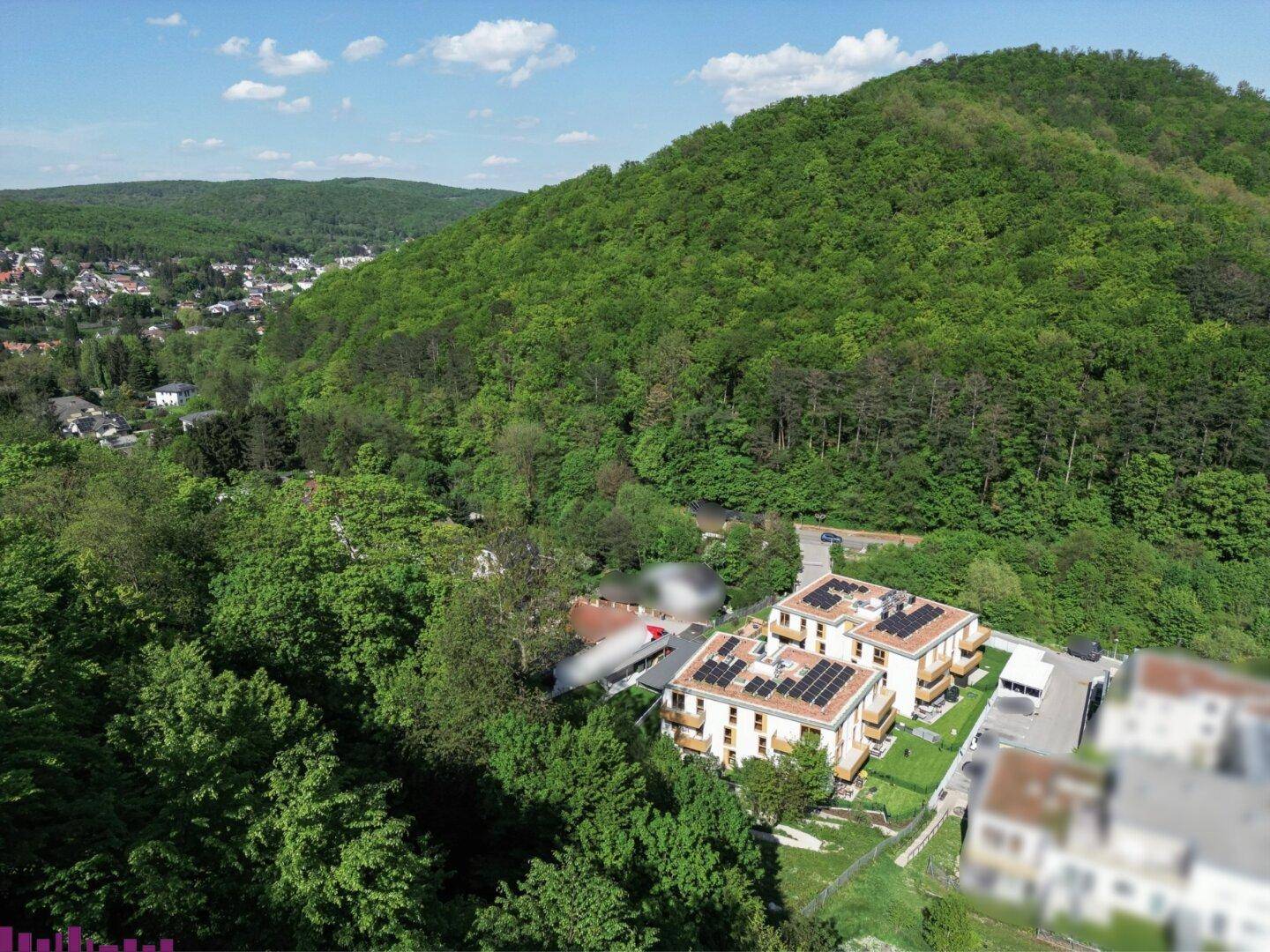 Weitläufige Luftaufnahme von modernen Wohngebäuden mit Solaranlagen auf den Dächern, umgeben von üppiger Natur.