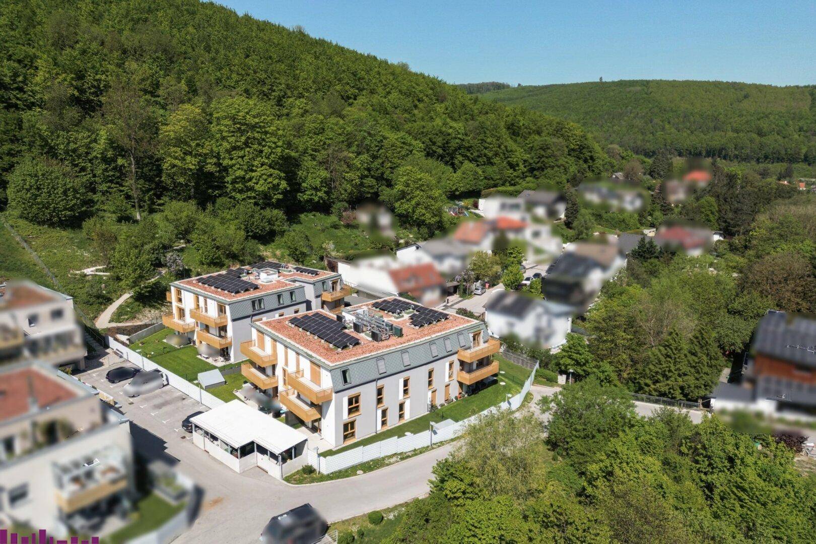 Moderne Wohngebäude mit Photovoltaikanlagen auf den Dächern, umgeben von Grünflächen und einer Wohnsiedlung.
