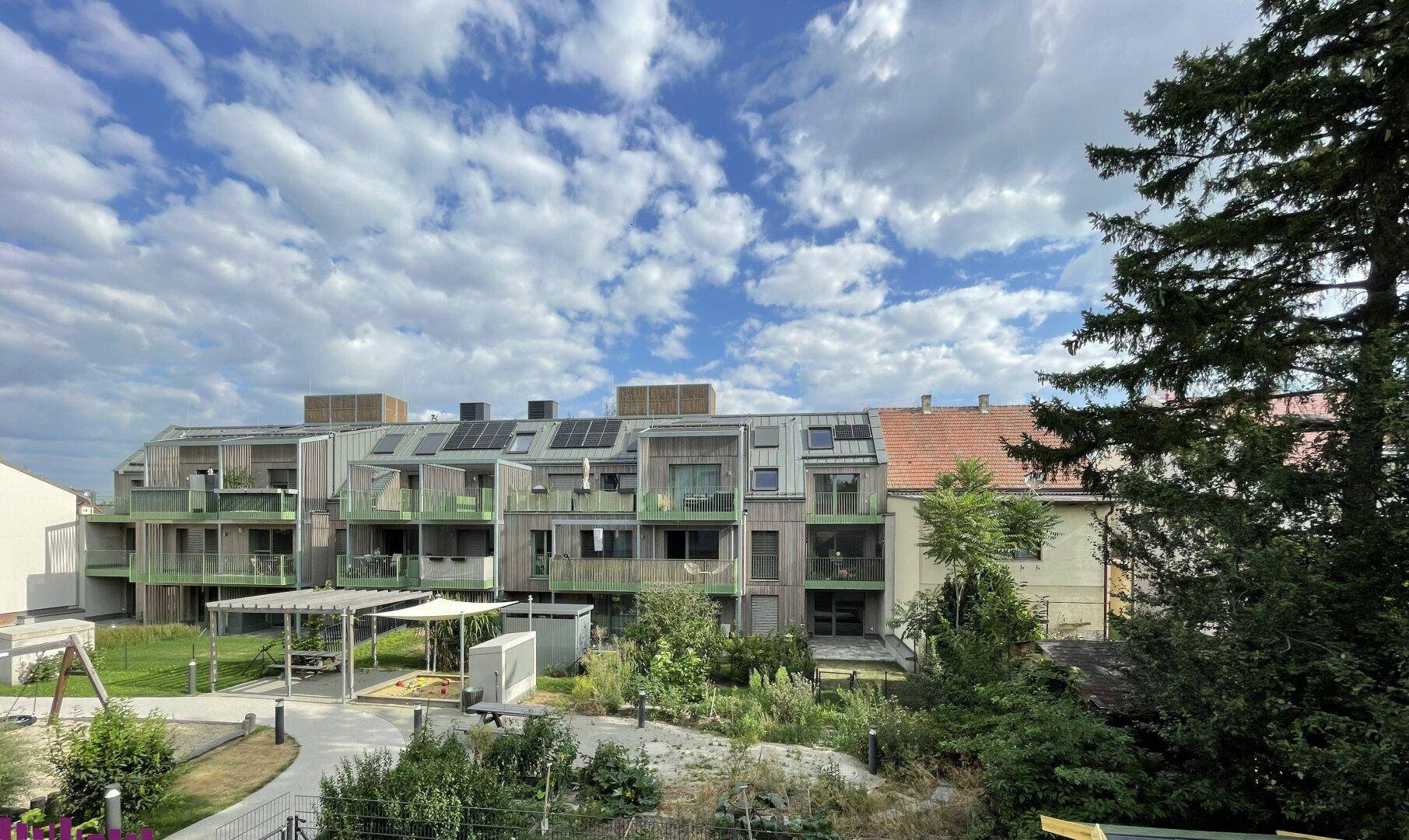 Blick auf die moderne Wohnanlage mit begrüntem Innenhof und Spielplatz unter bewölktem Himmel.