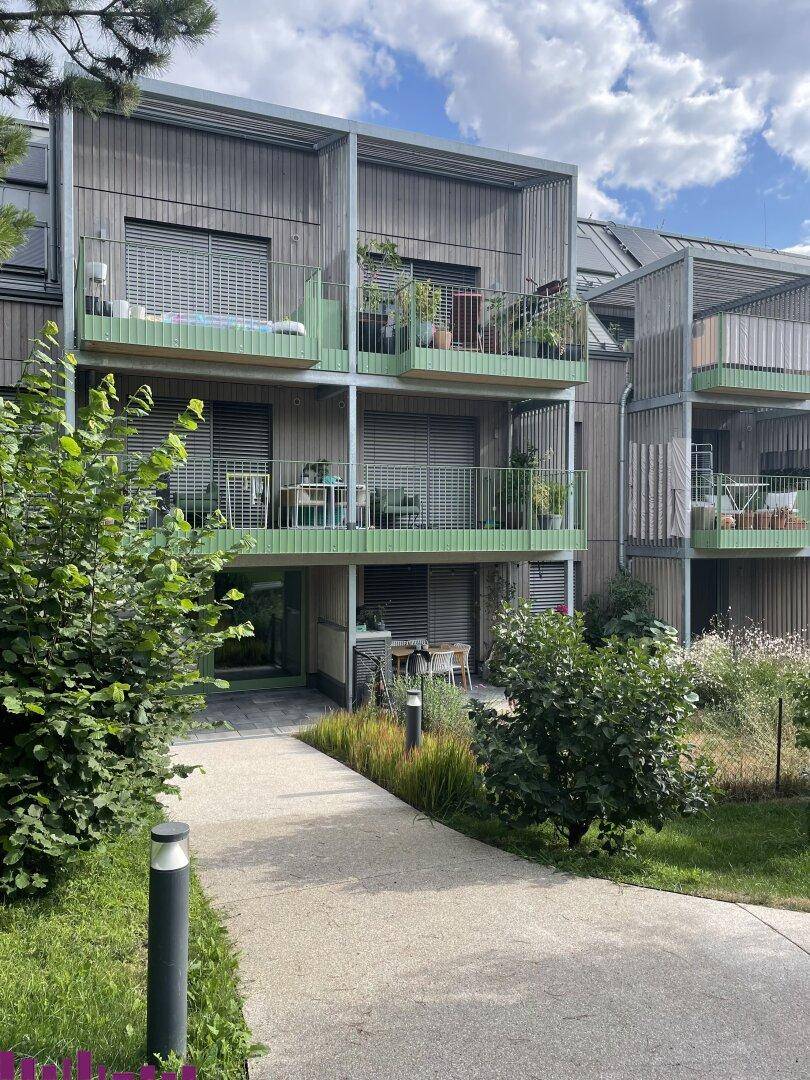 Moderne Wohnanlage mit Holzfassade und Balkonen, umgeben von einer gepflegten Gartenlandschaft mit Wegen.