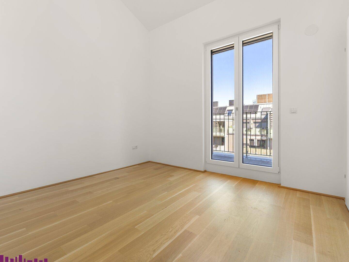 Helles, leeres Zimmer mit Holzboden und Zugang zu einem französischen Balkon, ideal als Schlafzimmer.
