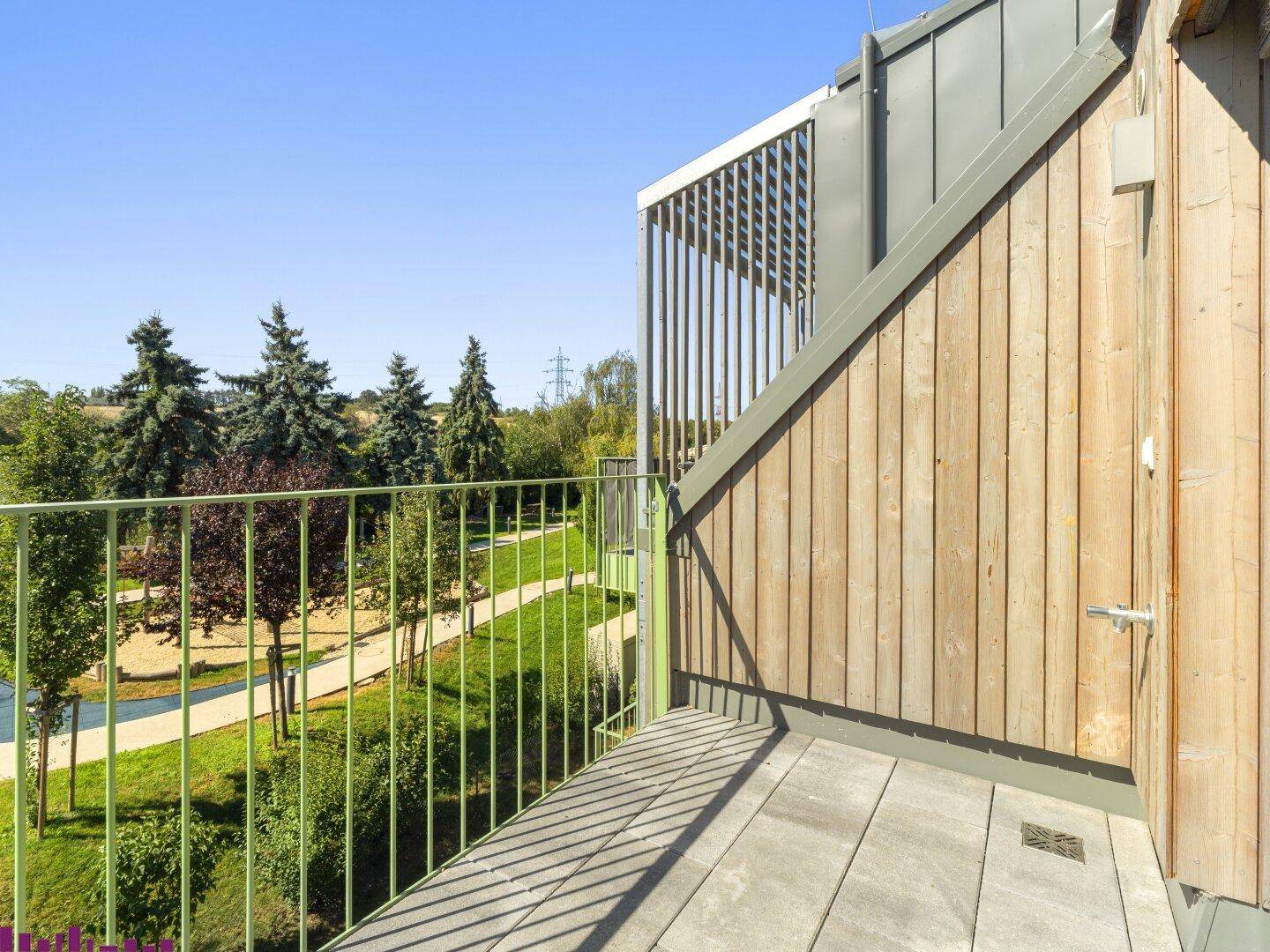 Kleiner Balkon mit Fliesenboden und Holzwandverkleidung, bietet einen ruhigen Blick ins Grüne.
