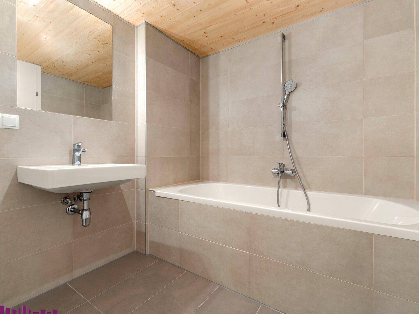 Modernes Badezimmer mit beigefarbenen Fliesen, Badewanne und Holzdecke, ausgestattet mit einem Waschbecken.
