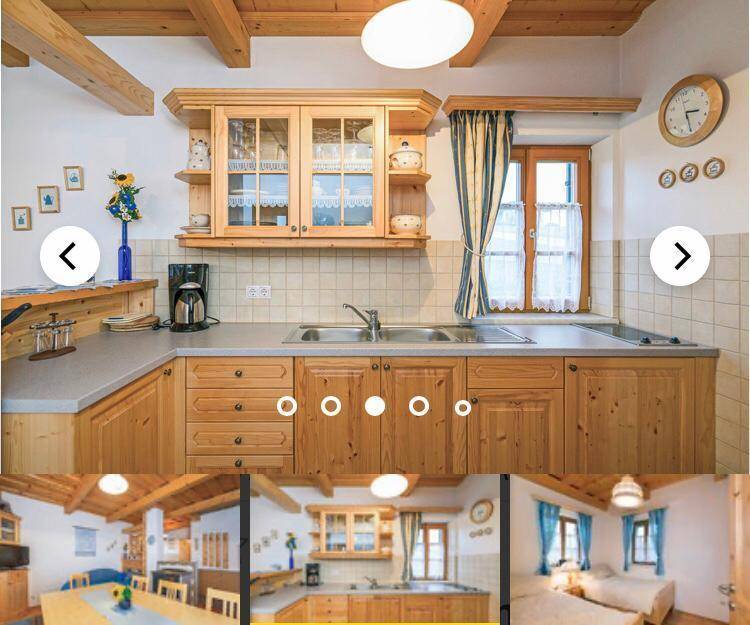 Traditionelle Holzküche mit Doppelspüle, gefliestem Spritzschutz und karierten Vorhängen am Fenster.