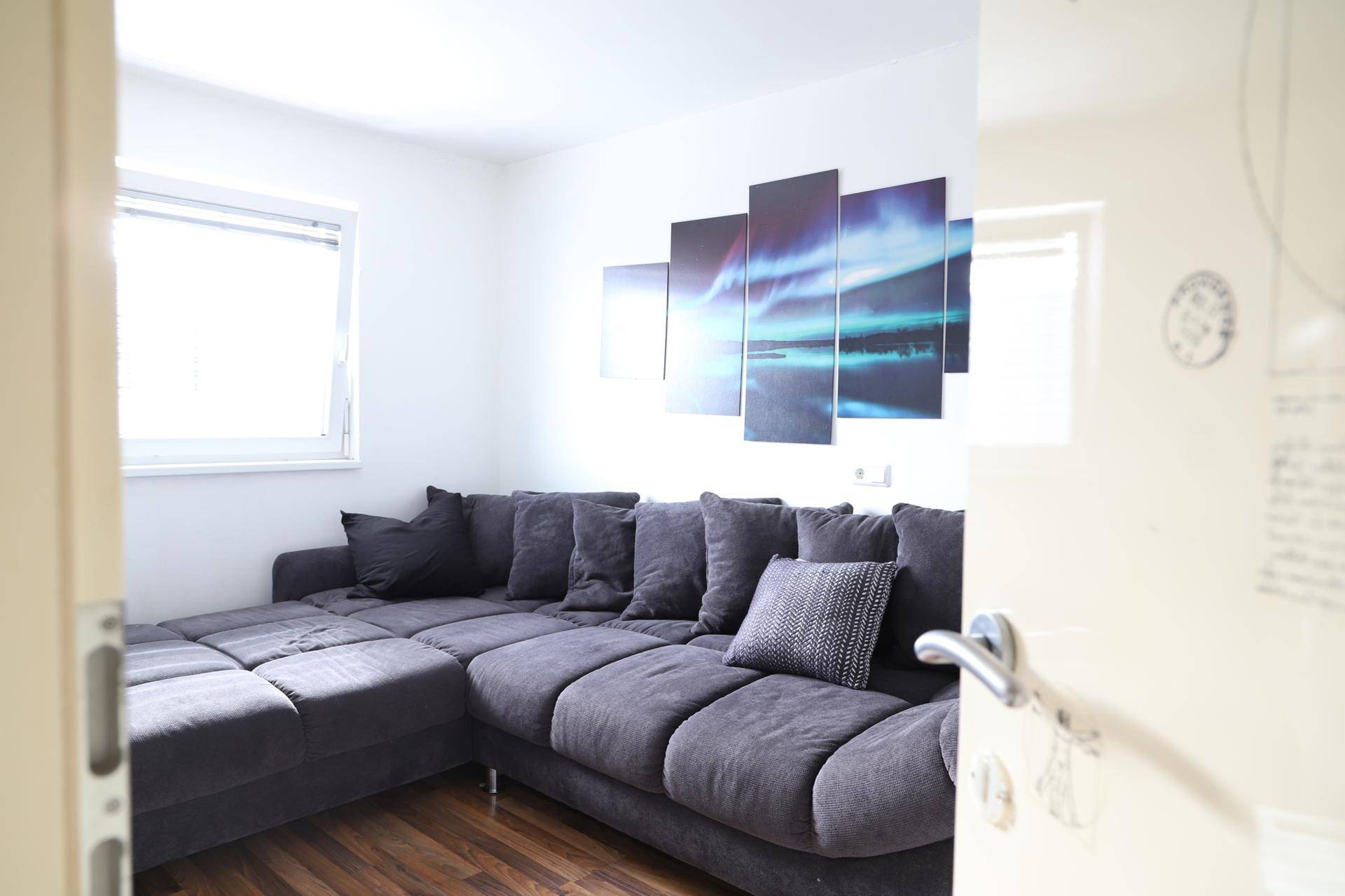 Gemütliches Zimmer mit großem grauen Ecksofa, Holzboden und moderner Wanddekoration.