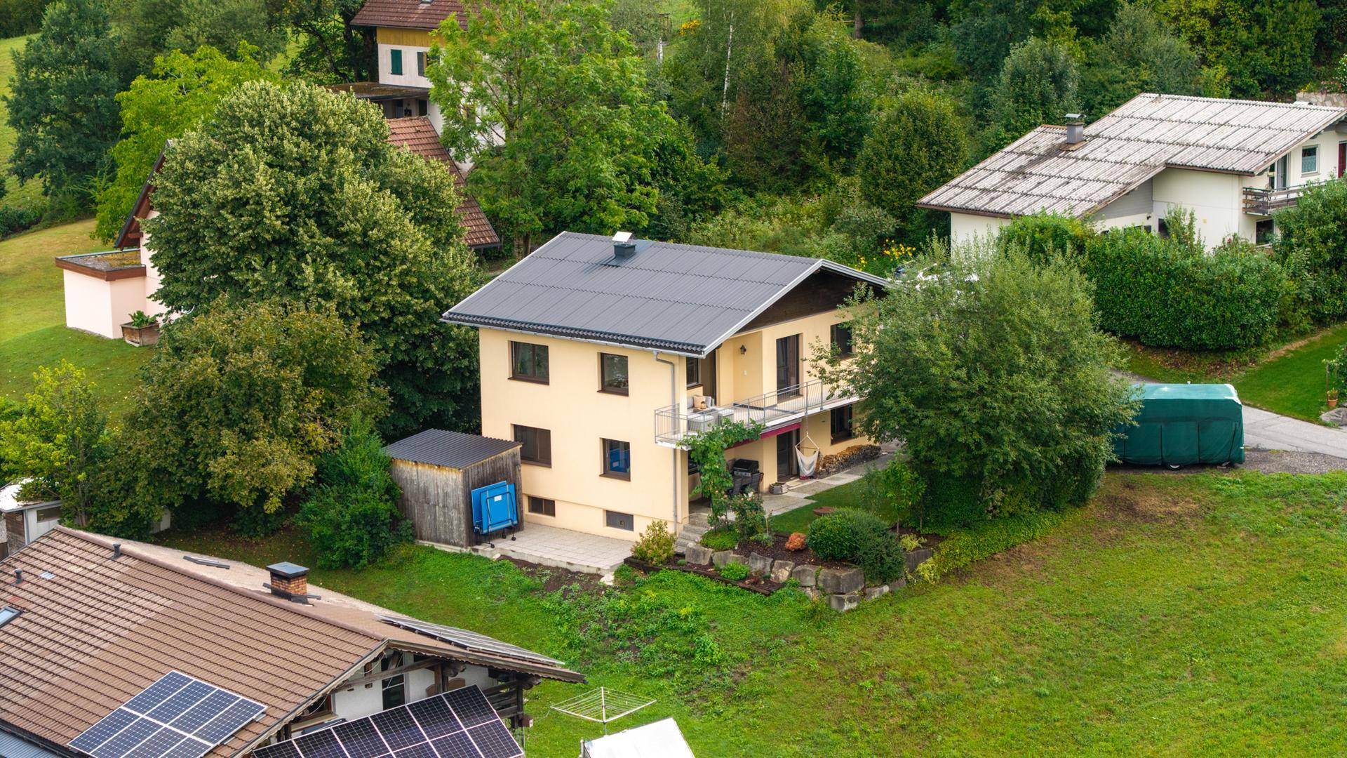 Luftaufnahme eines Einfamilienhauses mit Garten, Nebengebäude und umgeben von viel Grün.