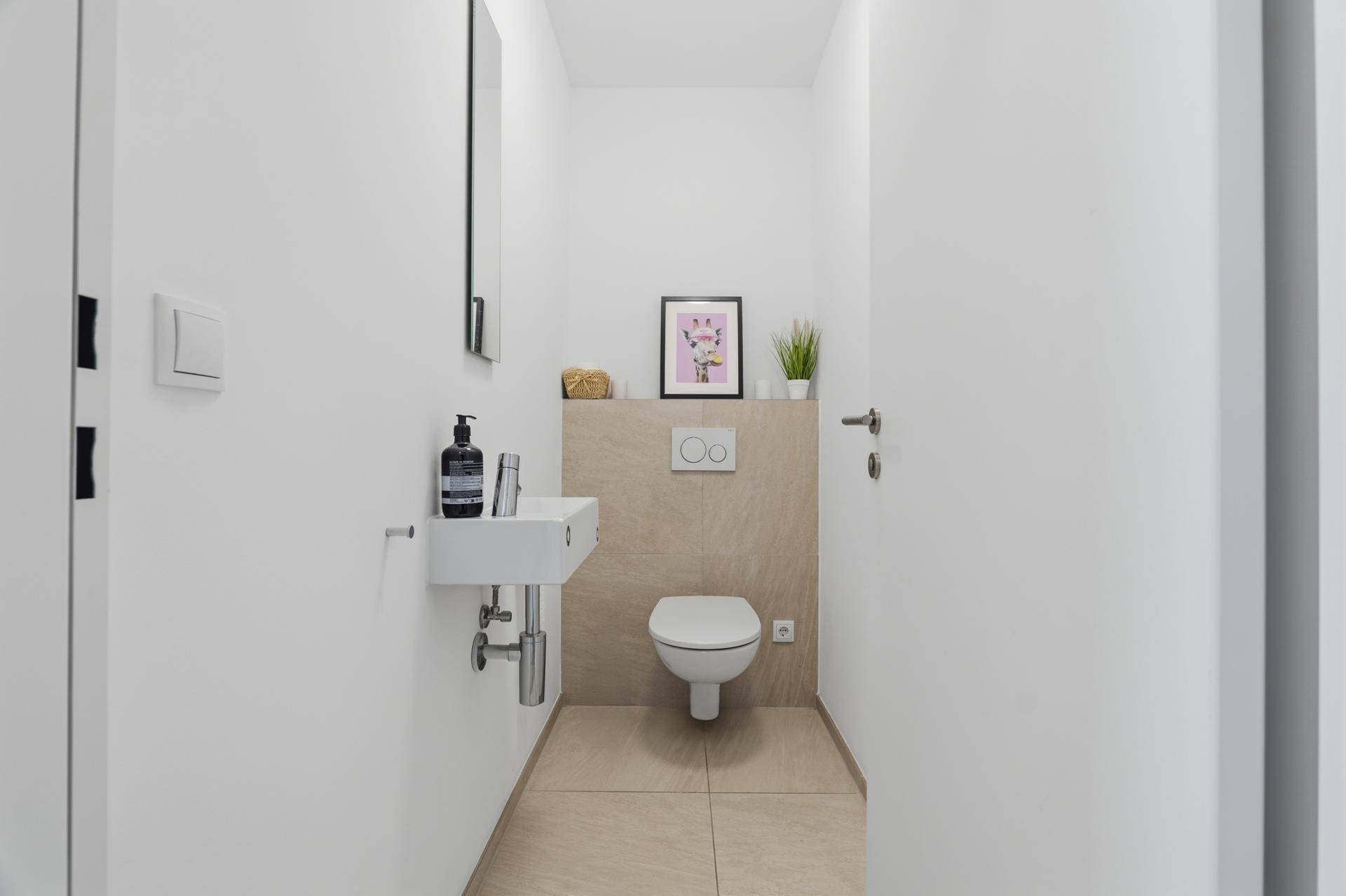Kompaktes Gäste-WC mit modernem Waschbecken und Wand-WC, halbhoch gefliest.