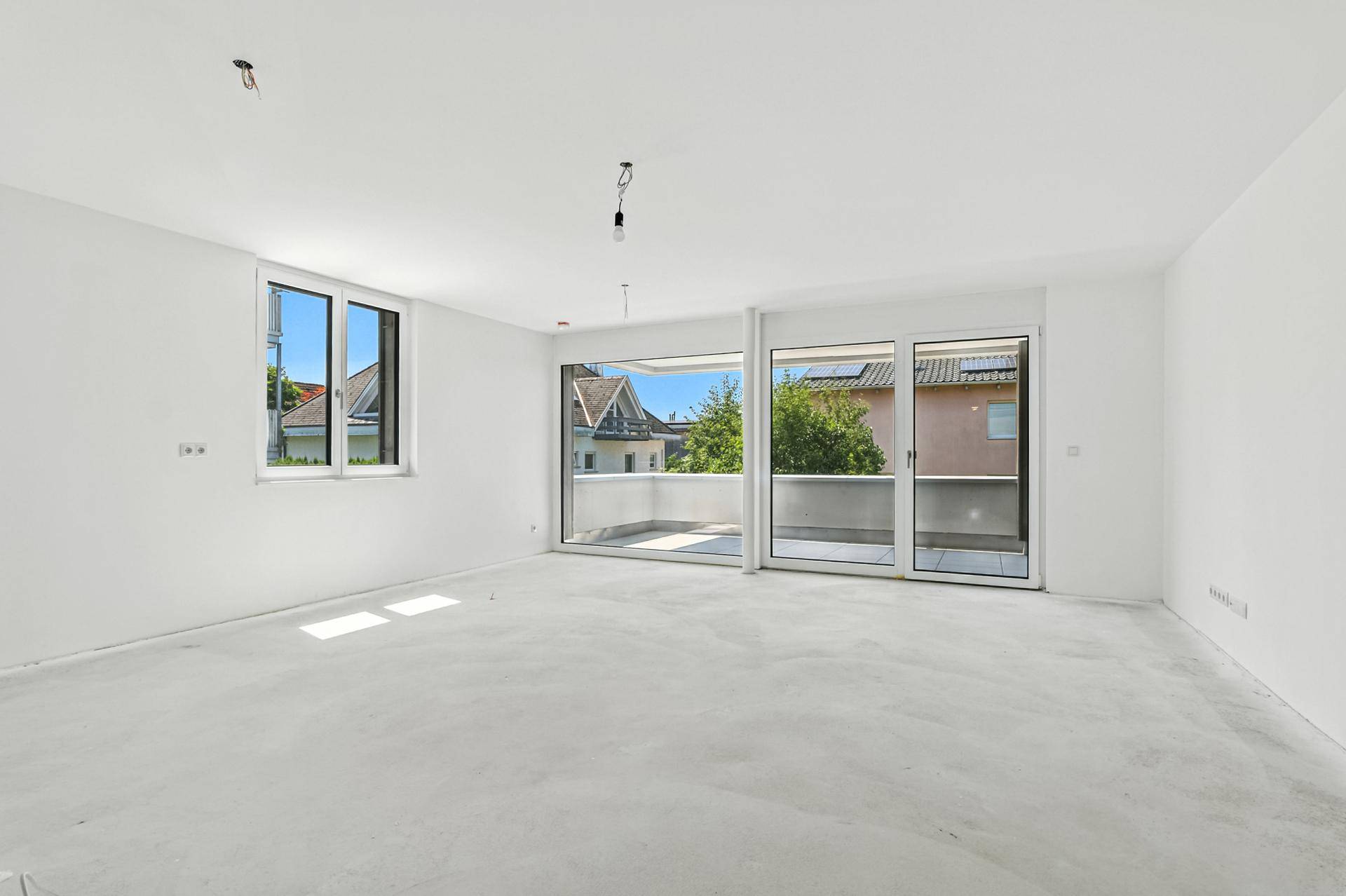 Leerer Raum im Rohbau mit Zugang zu einem Balkon und viel Tageslicht.