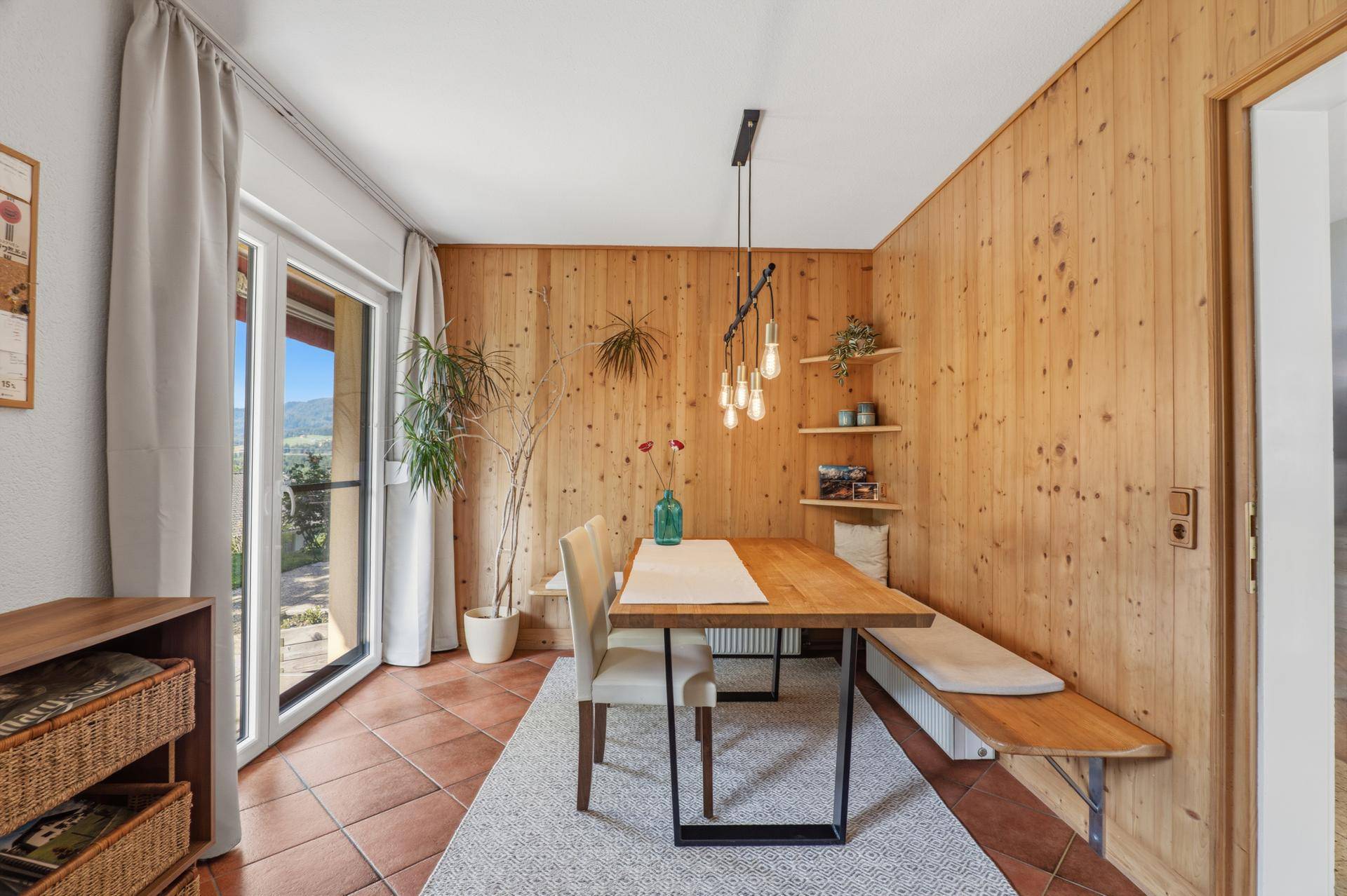 Essbereich mit Holztisch, Sitzbank und Zugang zu einem Balkon mit schöner Aussicht.