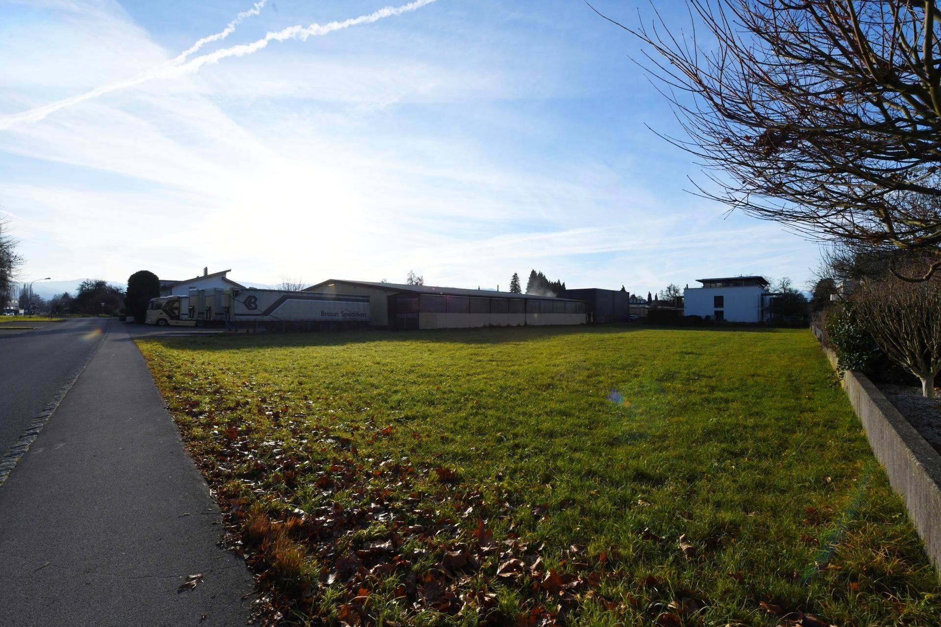 Blick auf ein sonniges, unbebautes Grundstück neben einer Straße mit umliegenden Gebäuden.