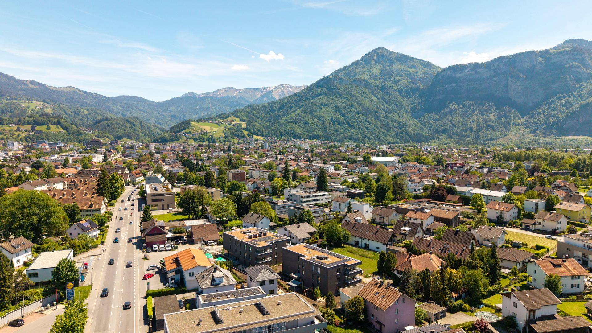 Panoramablick aus der Vogelperspektive auf eine Wohnsiedlung mit imposanten Bergen im Hintergrund.