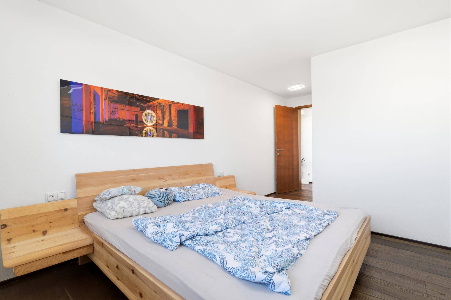 Helles Schlafzimmer mit Holzbett und modernem Kunstwerk an der Wand.