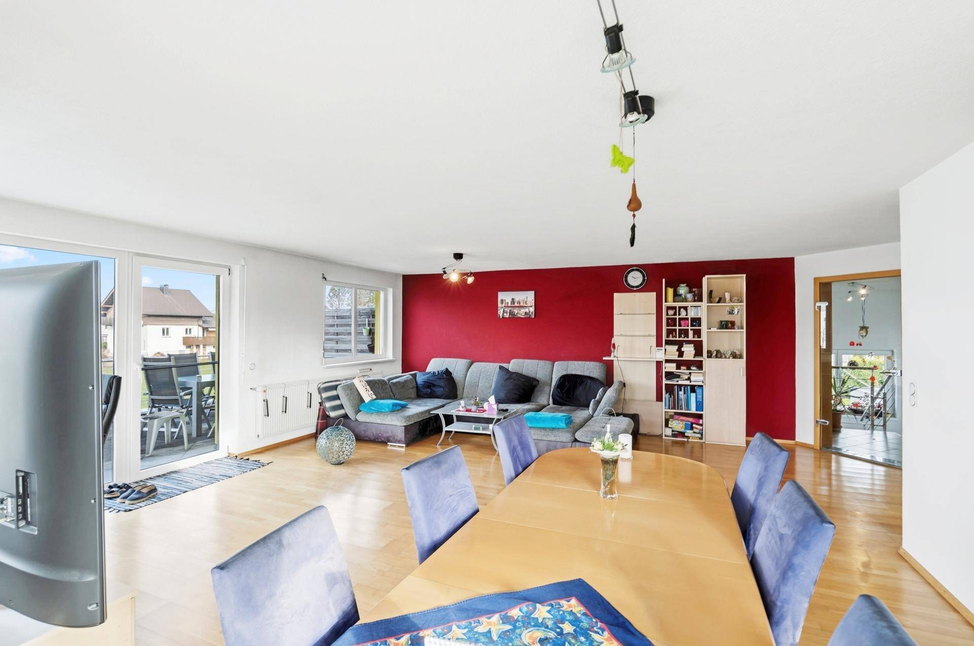 Geräumiger Wohn-Essbereich mit roter Akzentwand, Holzboden und Zugang zur Terrasse.