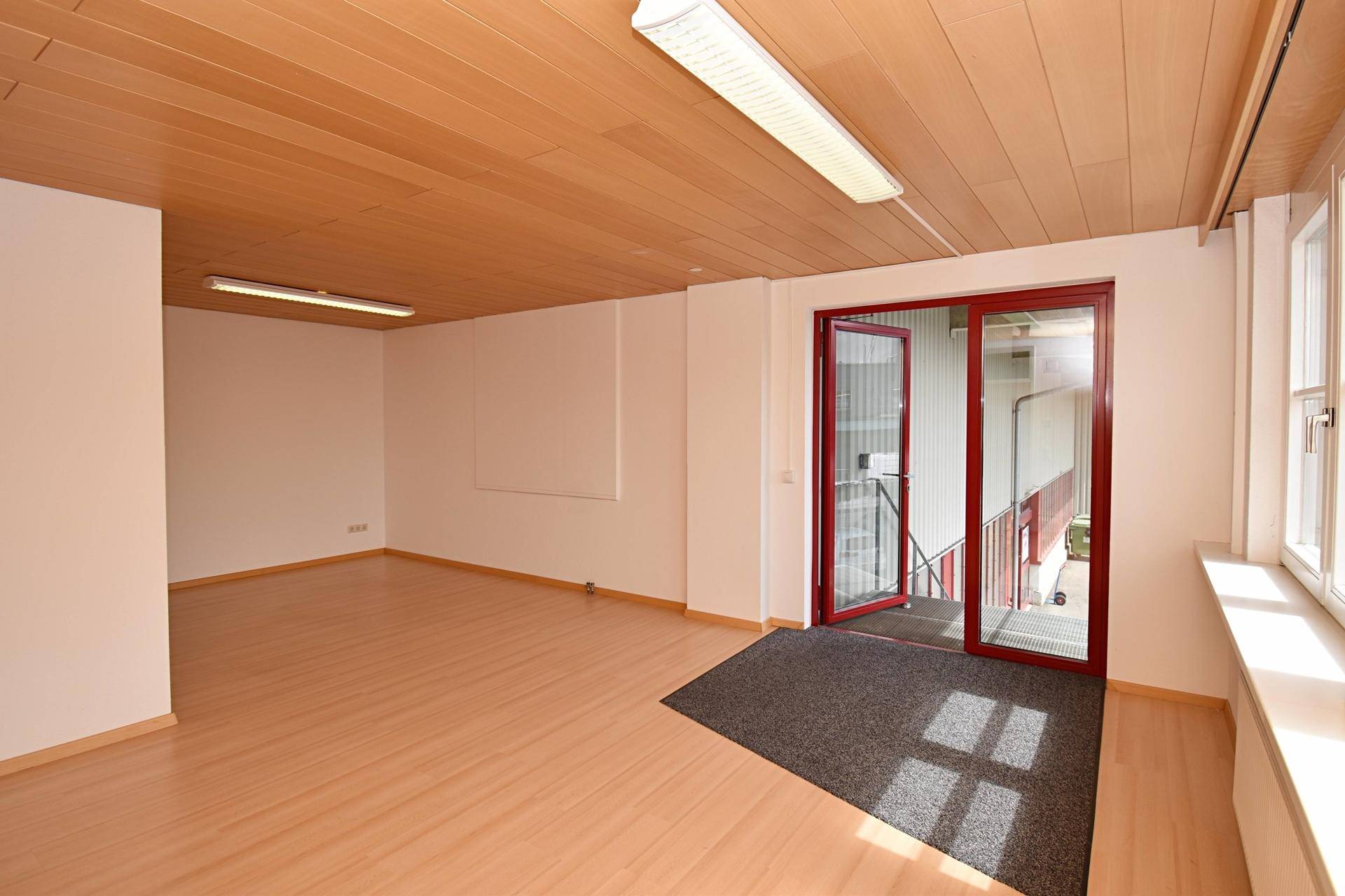 Geräumiger, heller Raum mit Laminatboden, Holzdecke und Zugang zur Außentreppe.