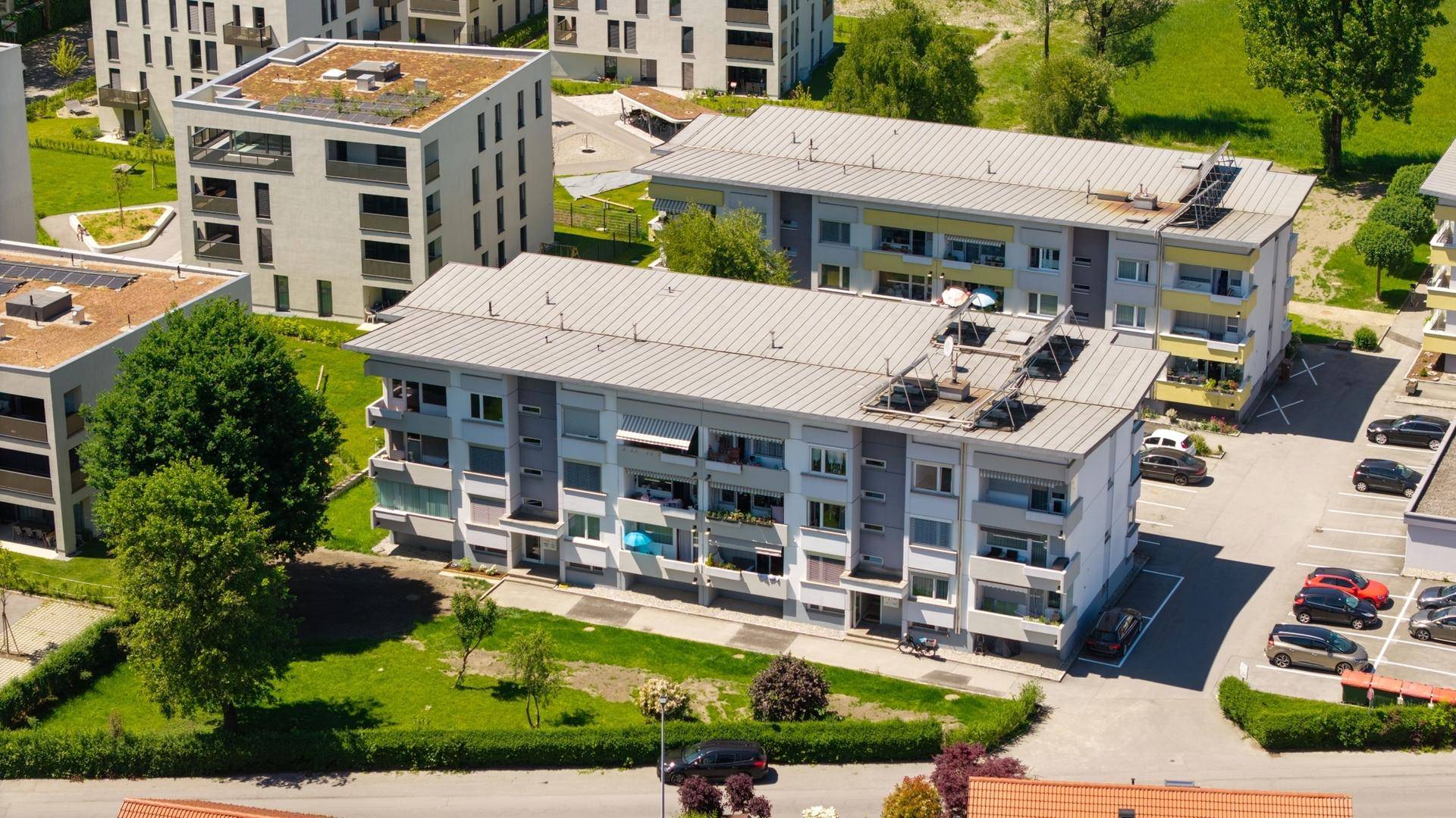 Luftaufnahme von Wohngebäuden mit Flachdächern und Parkplätzen in grüner Umgebung.