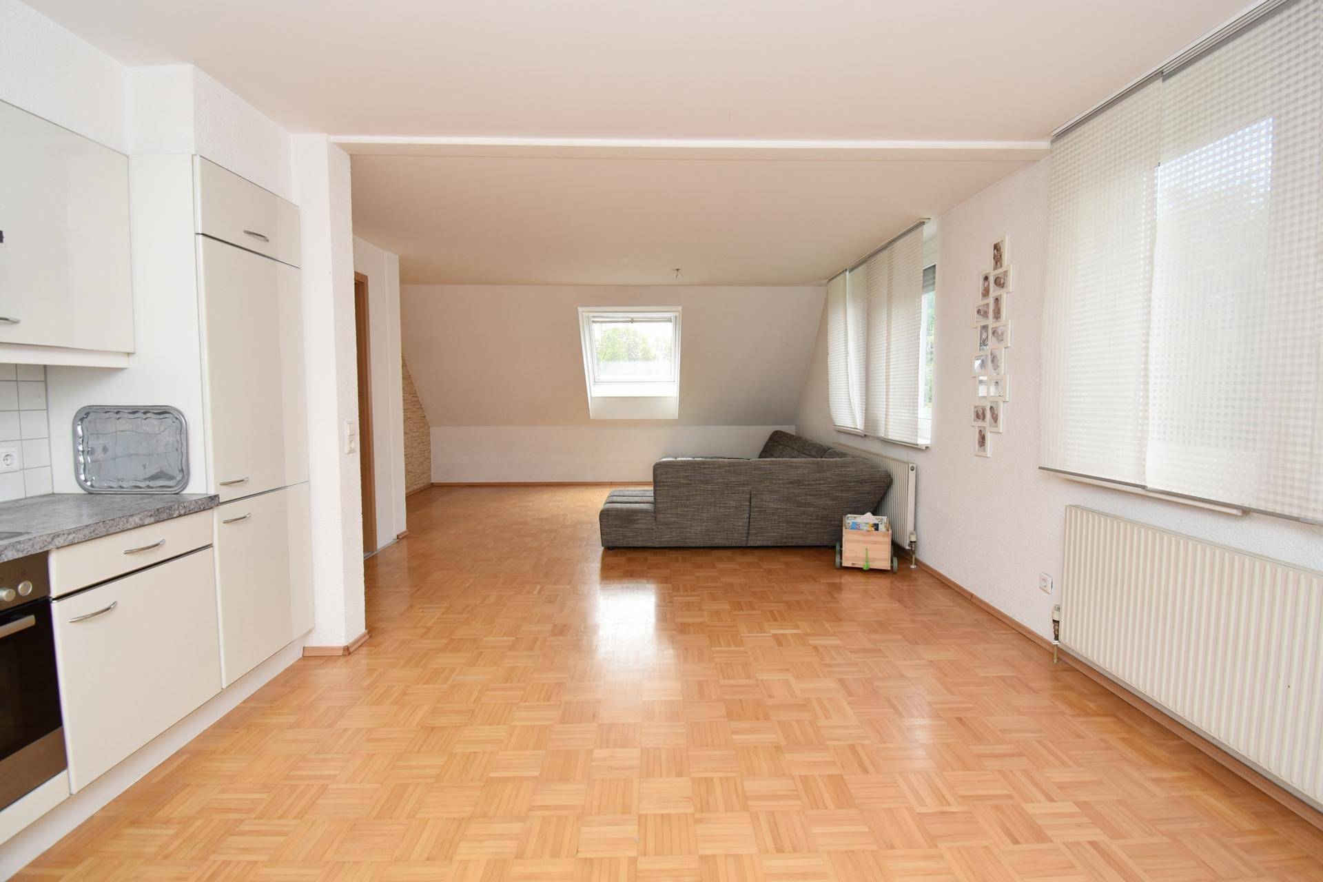 Geräumiger Wohnbereich mit offener Küche, Parkettboden und großen Fenstern.