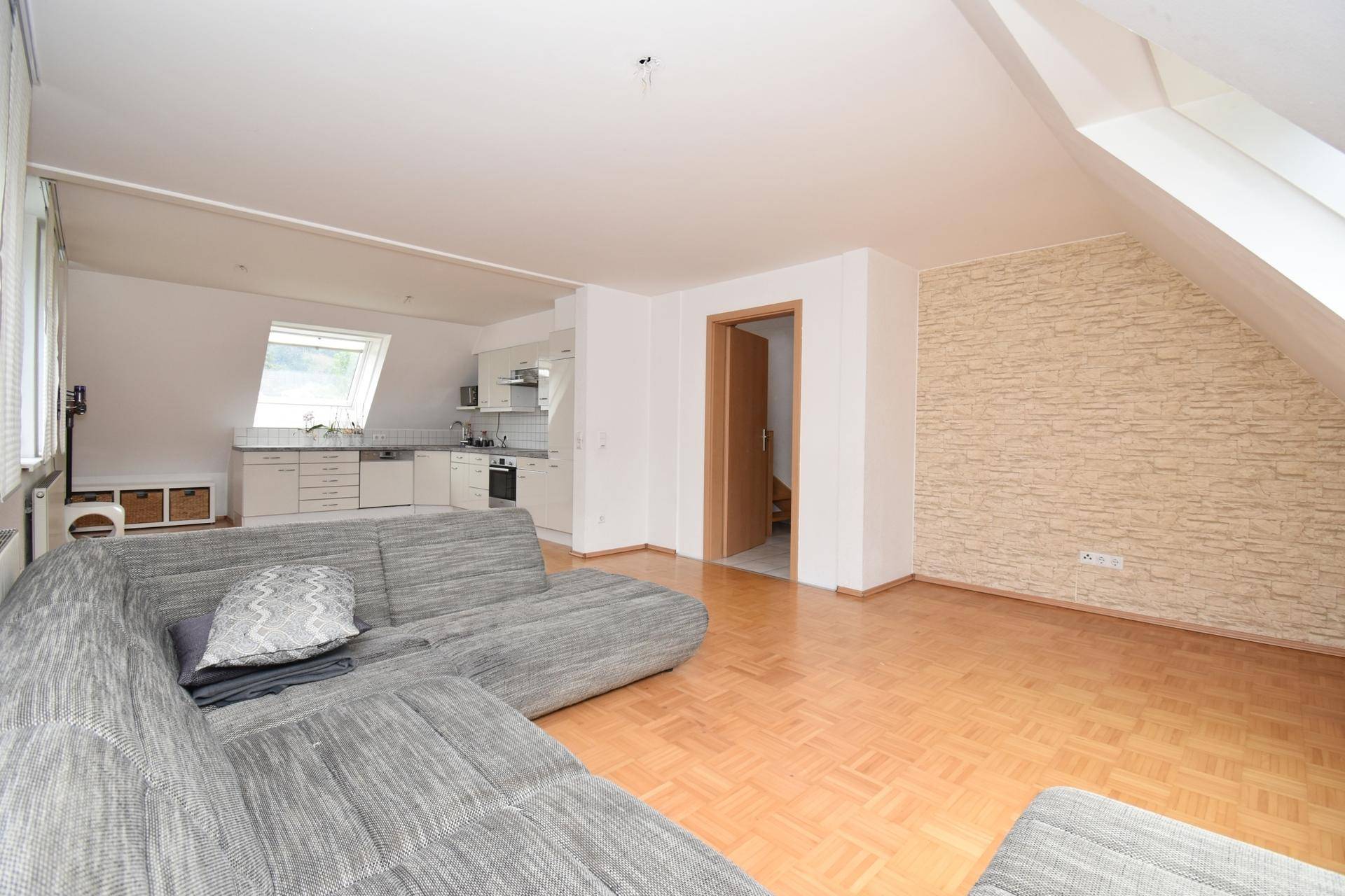 Offener Wohnbereich mit gemütlichem Sofa, Parkettboden und strukturierter Wand.