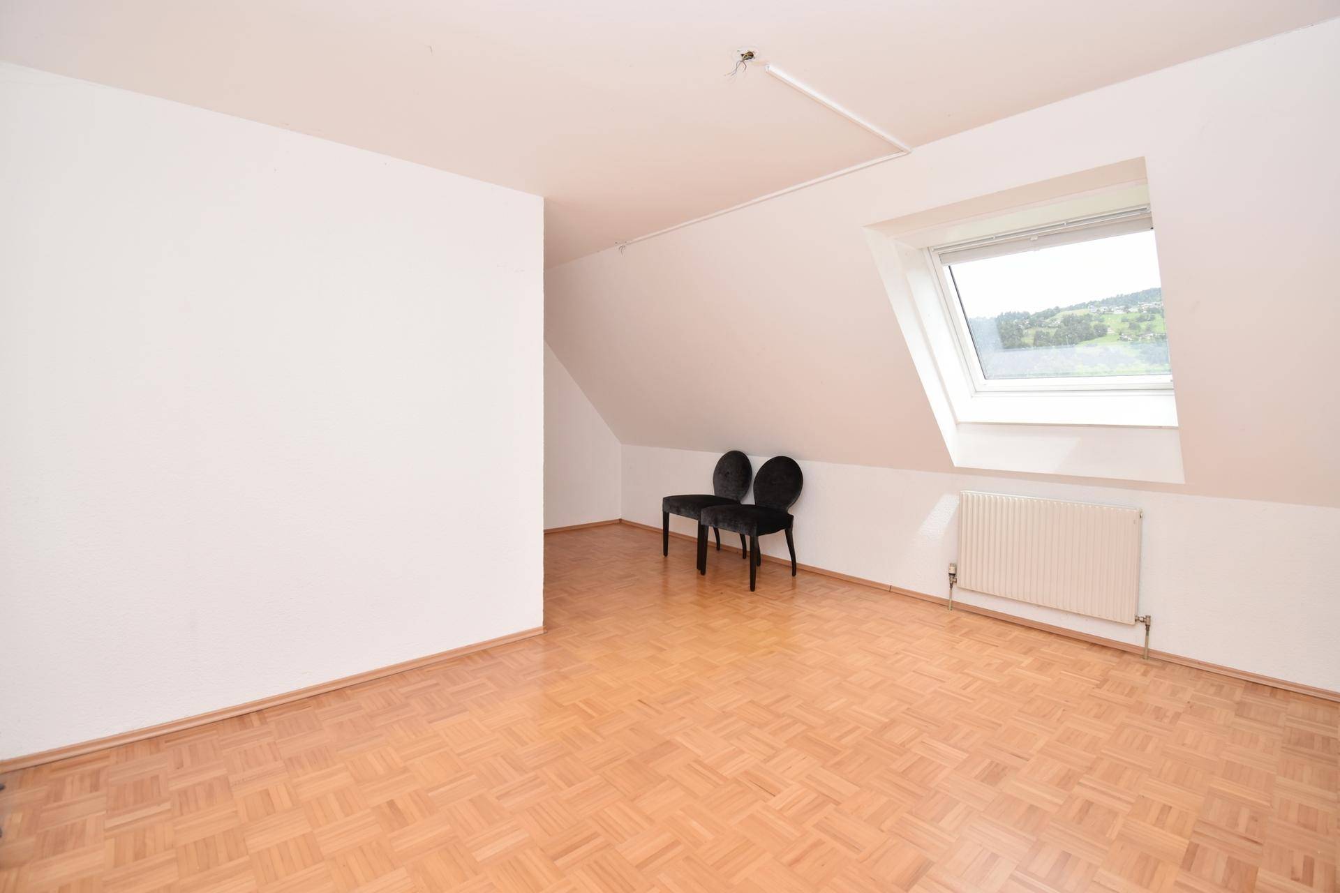 Helles Schlafzimmer mit Parkettboden, Dachfenster und Blick ins Grüne.