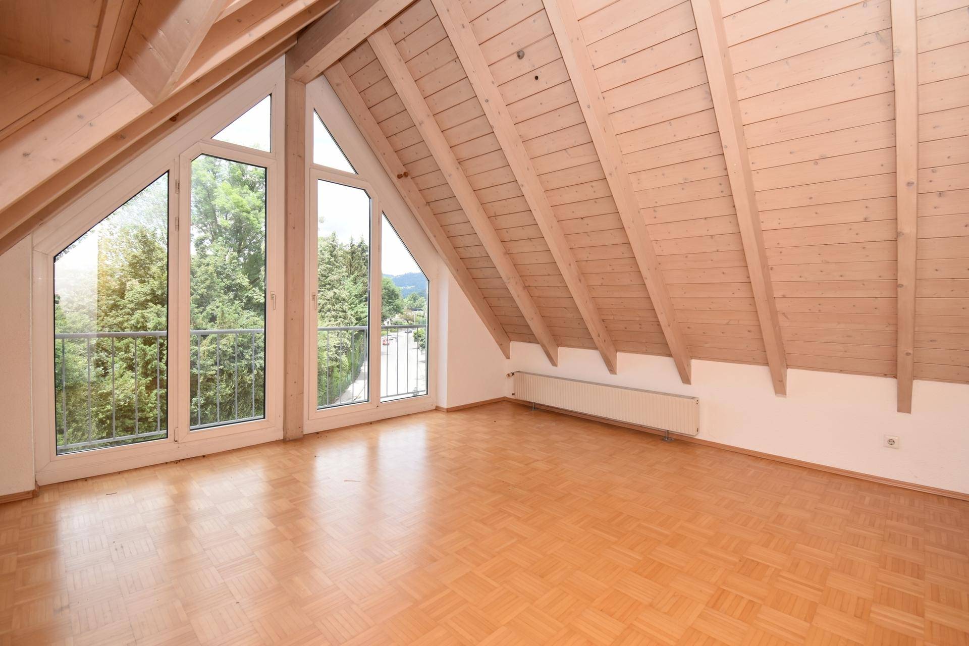 Geräumiges Wohnzimmer mit Holzdachschräge, Parkettboden und Balkonzugang.