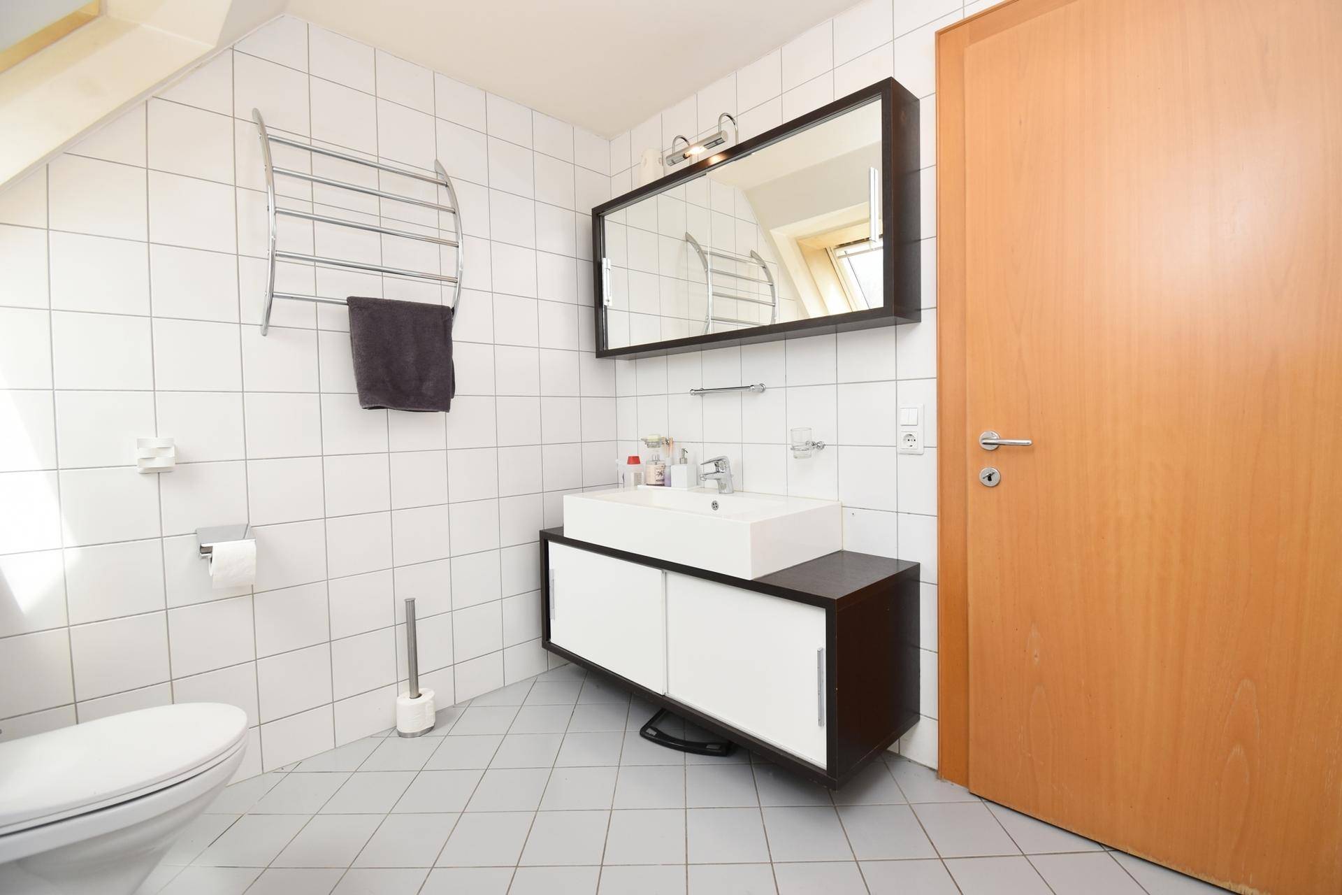 Modernes Badezimmer mit Waschtisch, Spiegel und weißen Fliesen.