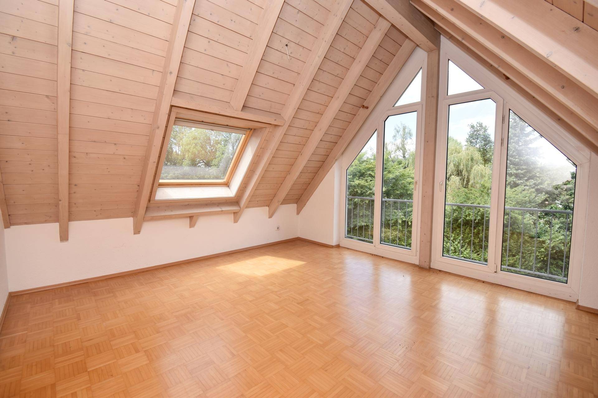 Helles Wohnzimmer im Dachgeschoss mit Holzbalken und großen Fenstern.