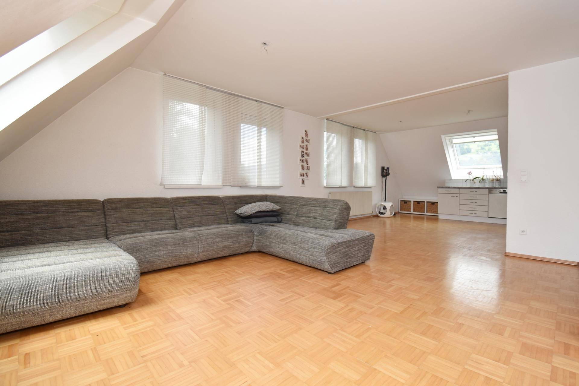 Weitläufiger Wohnbereich mit Parkettboden, großem Sofa und Blick zur Küche.