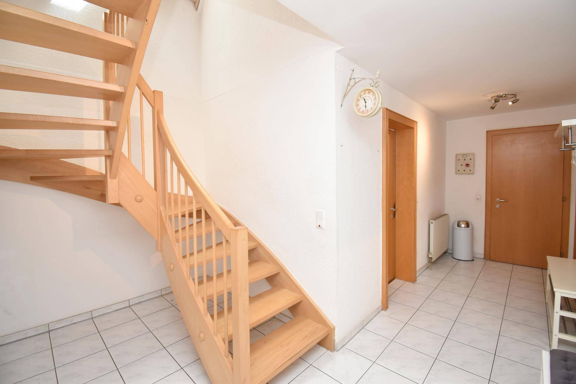 Eingangsbereich mit Holztreppe, Fliesenboden und Garderobenbereich.