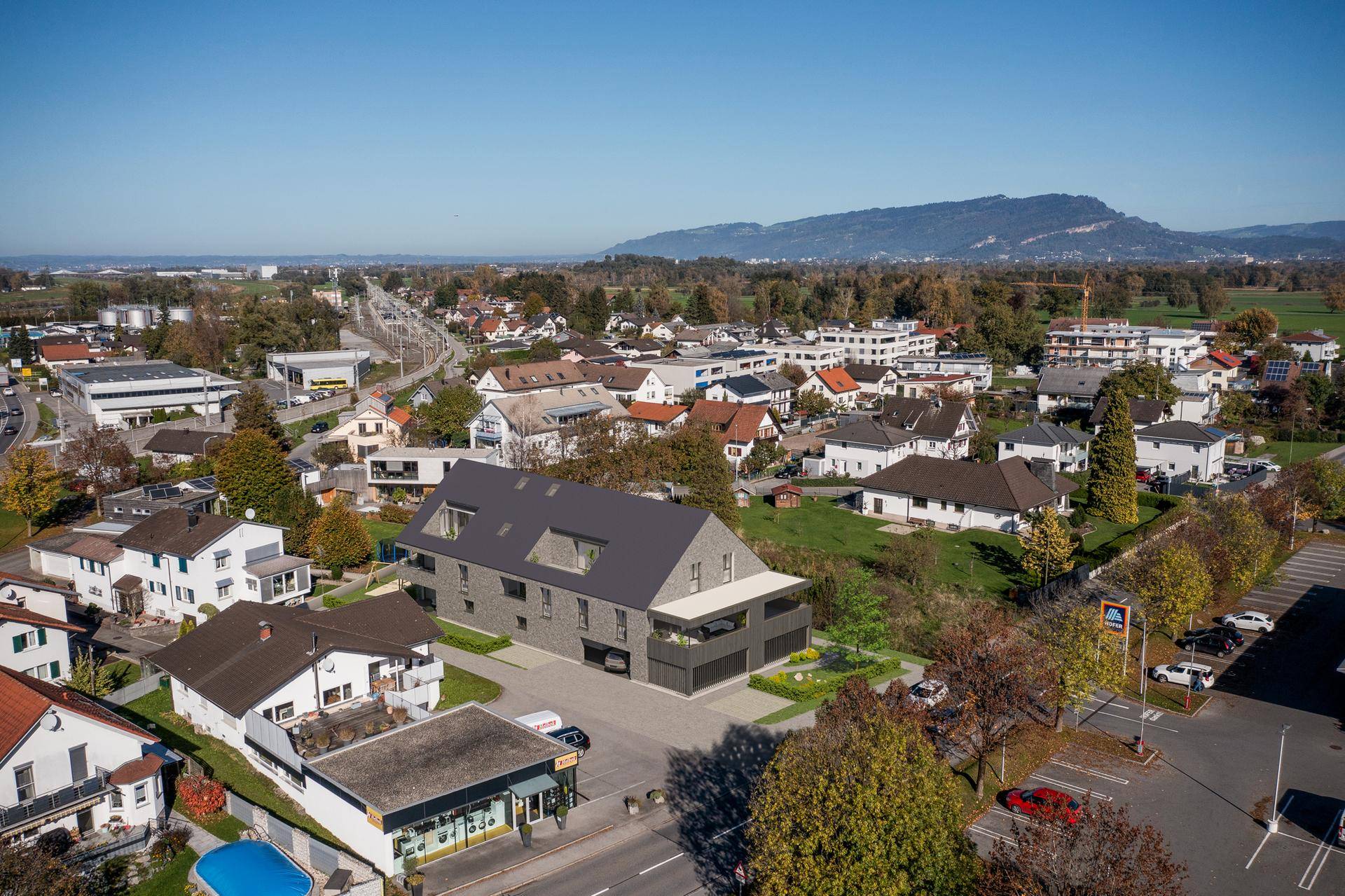 Luftaufnahme der Wohnanlage in städtischer Umgebung mit Bergblick und umliegender Infrastruktur.