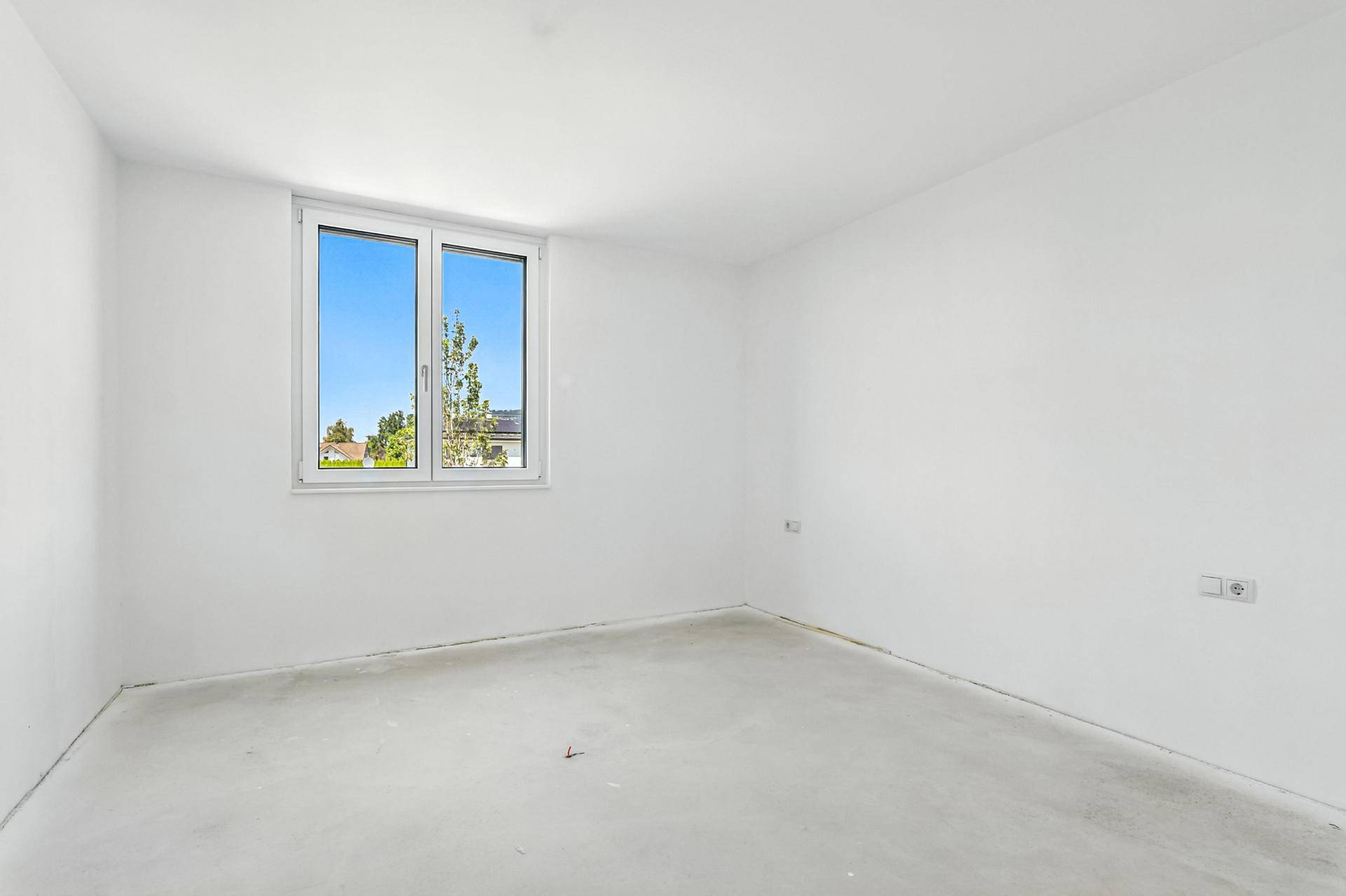 Leerer Raum mit weiß gestrichenen Wänden und einem Fenster, das viel Tageslicht hereinlässt.