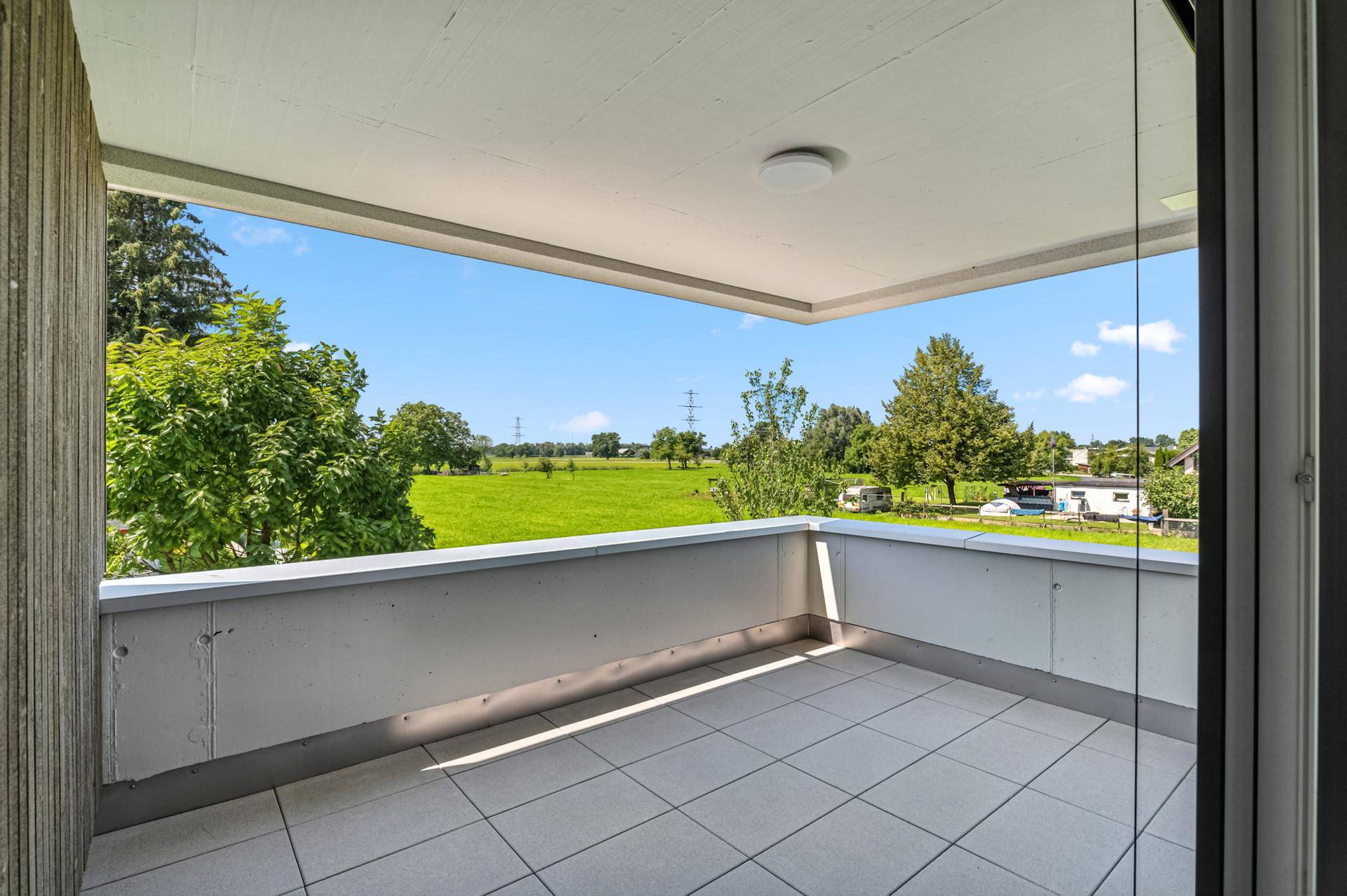 Geräumiger Balkon mit Fliesenboden und weitem Blick über grüne Felder und Landschaft.