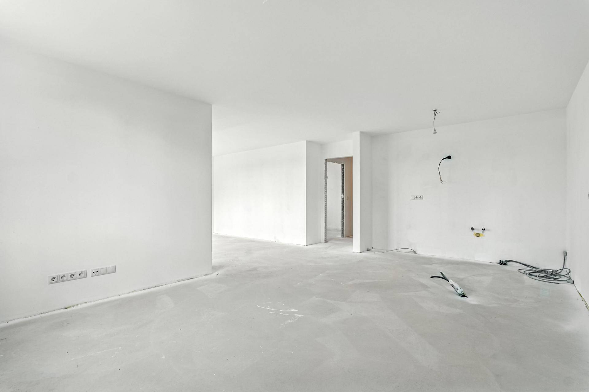 Unmöblierter Raum im Rohbauzustand mit weißen Wänden und Betonboden, bereit für den Ausbau.