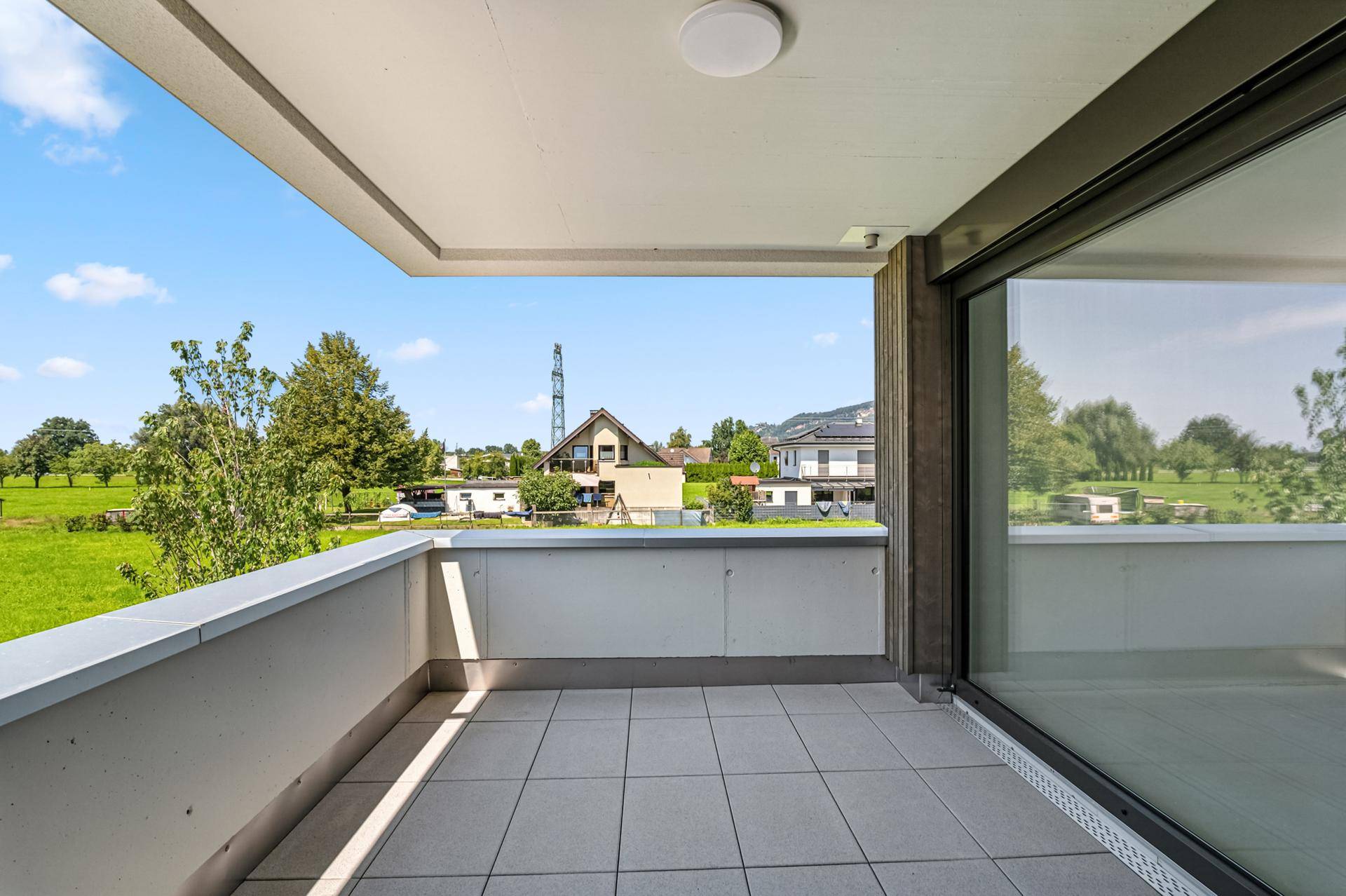 Heller Balkon mit Fliesen und Panoramablick auf die umliegende grüne Landschaft und Häuser.