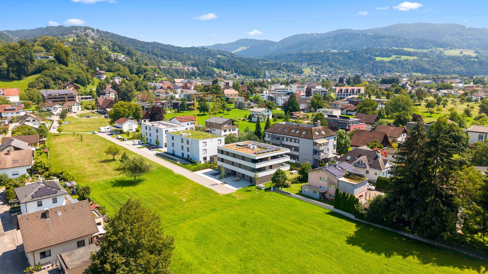 Weitläufige Luftaufnahme der Wohnsiedlung mit viel Grün und Bergen im Hintergrund.
