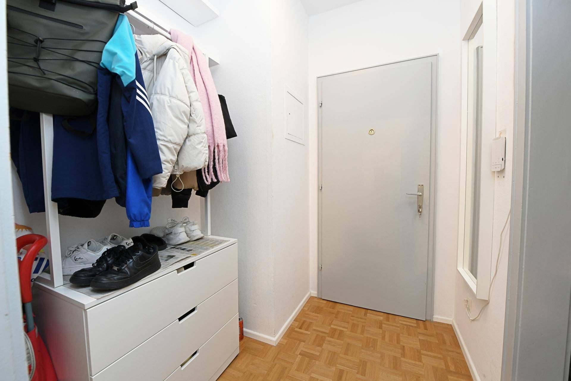 Eingangsbereich mit Garderobe, Schuhschrank und hellem Holzboden, der zur Wohnungstür führt.