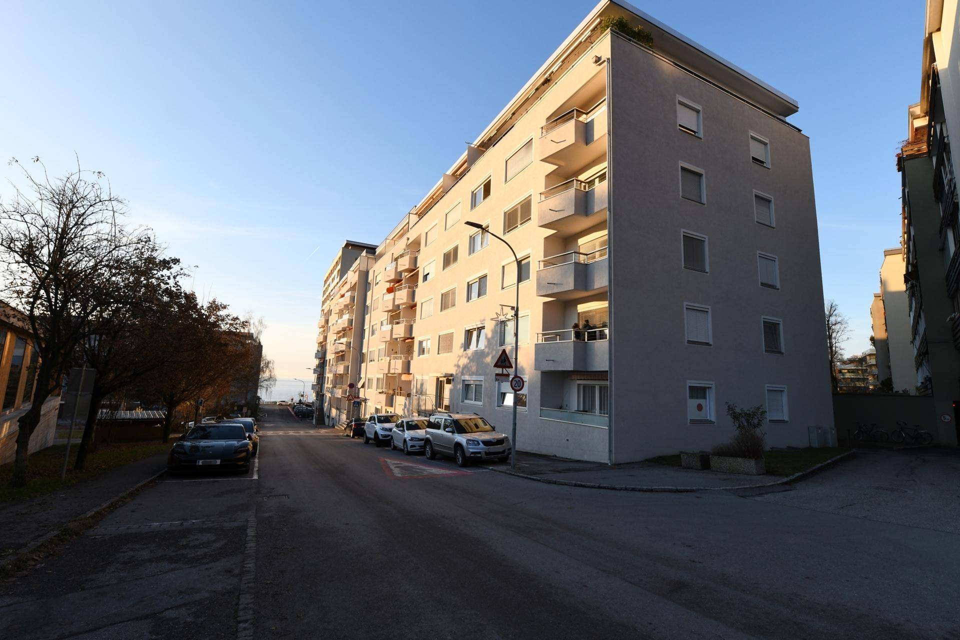 Modernes Mehrfamilienhaus mit Balkonen an einer ruhigen Straße bei Sonnenuntergang.