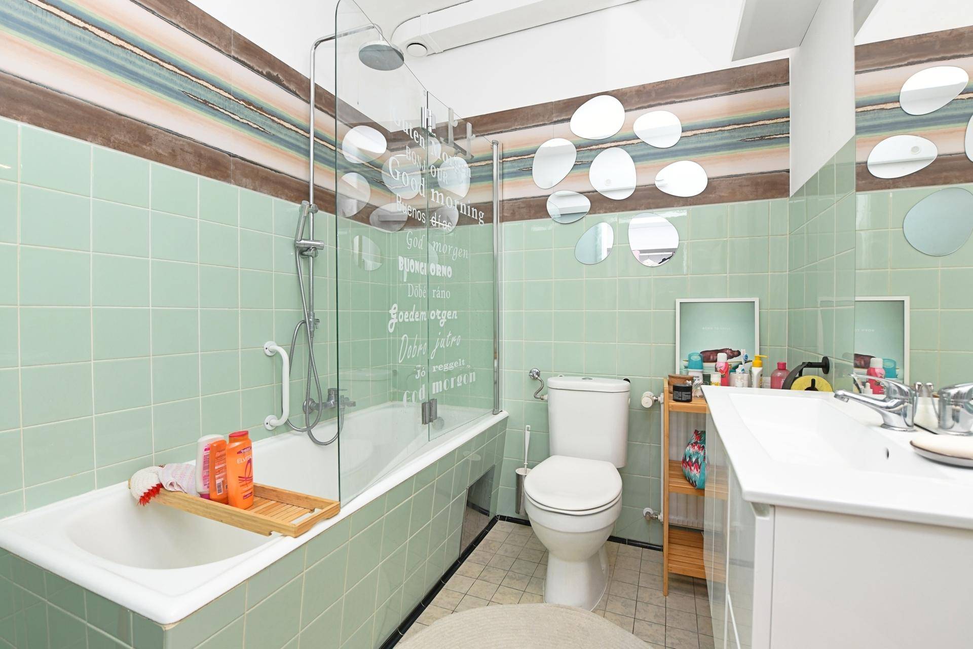 Badezimmer mit Badewanne, Dusche und mintgrünen Fliesen an den Wänden, ausgestattet mit einem Waschbecken.