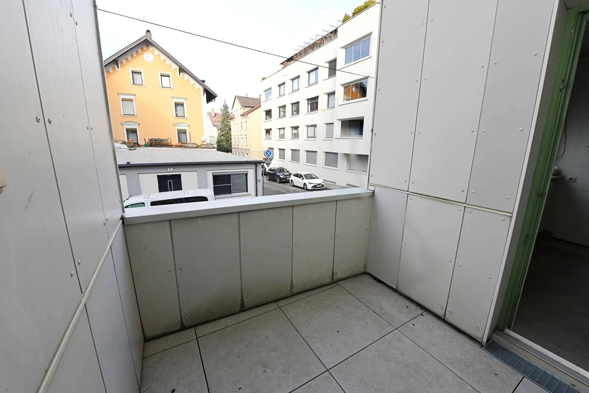 Kleiner Balkon mit Fliesenboden und Blick auf die umliegenden Gebäude und die Straße.