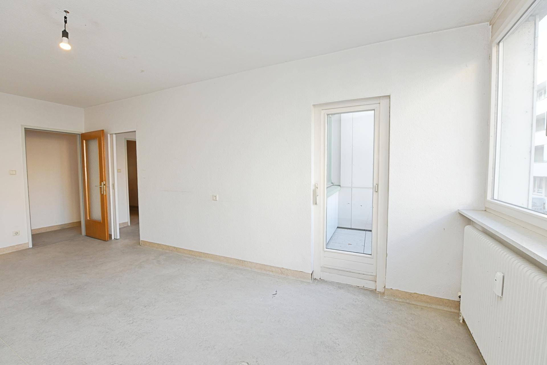 Heller Raum mit Betonboden und Zugang zu einem kleinen Balkon, ideal für ein Wohnzimmer.