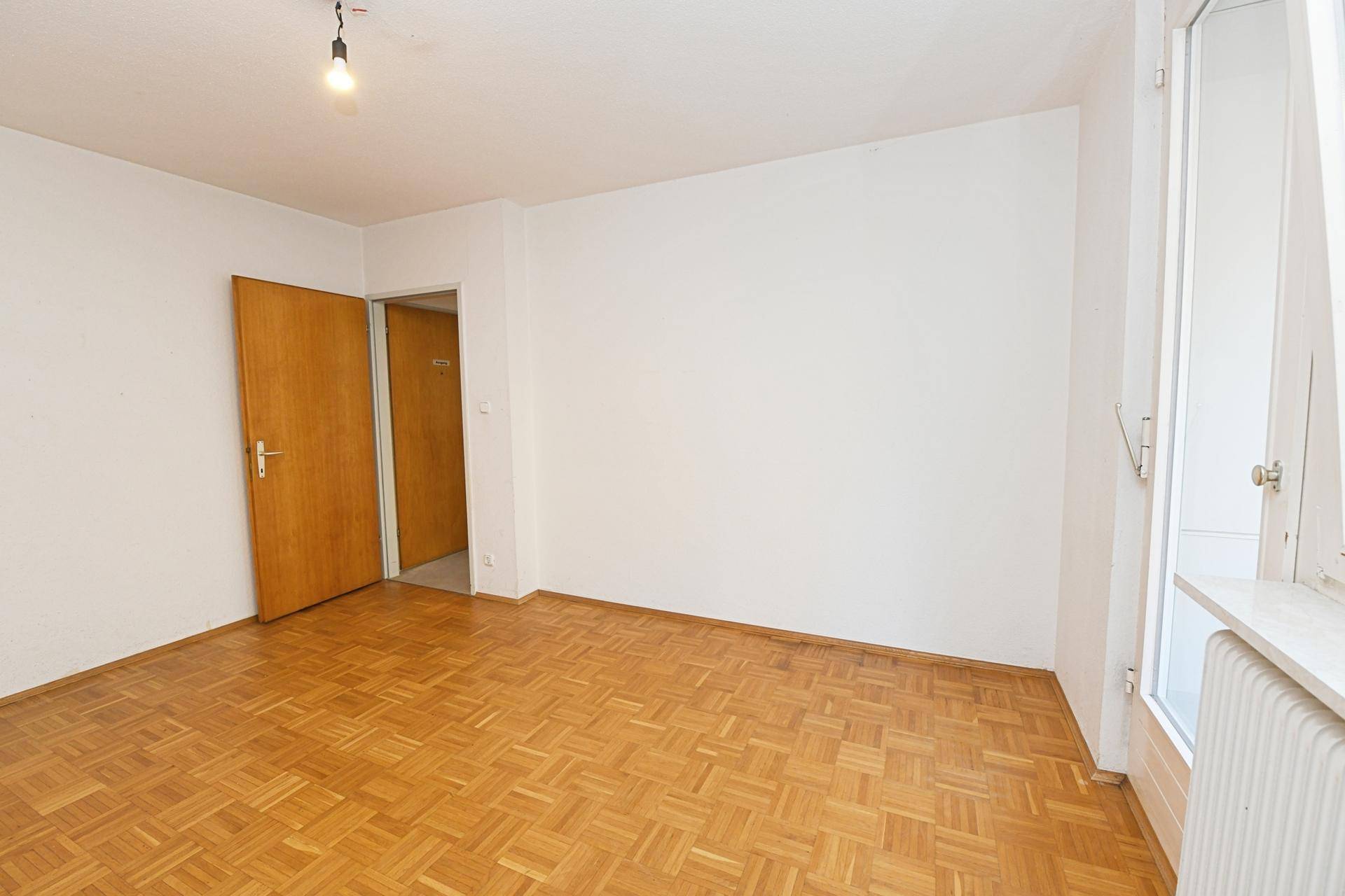 Heller Raum mit Fischgrätparkettboden und Fenster, ideal für ein gemütliches Wohnzimmer.