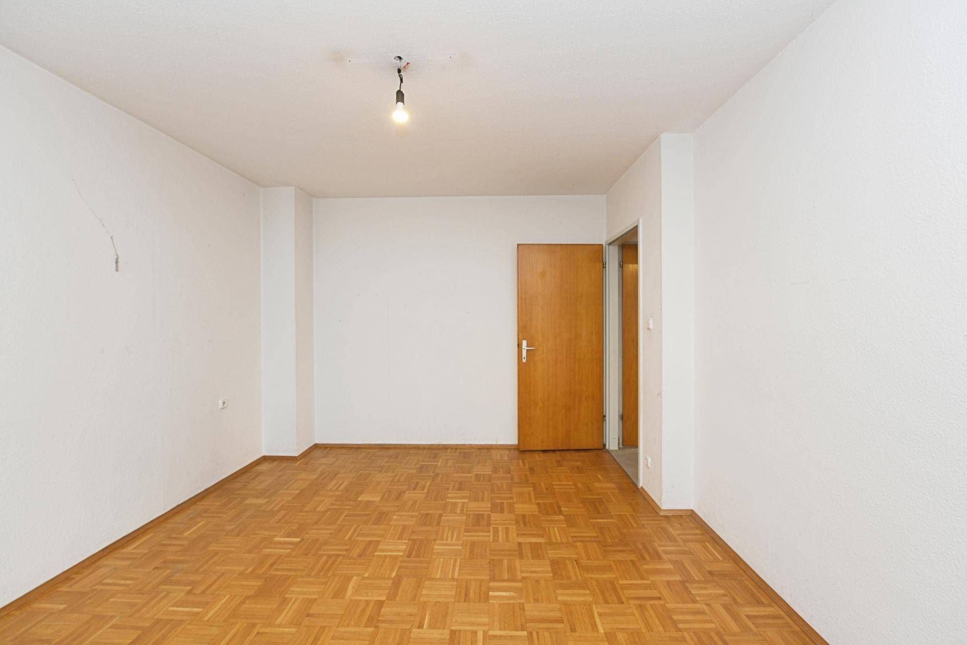 Geräumiges Zimmer mit Fischgrätparkettboden und Holztür, bereit zur individuellen Gestaltung.