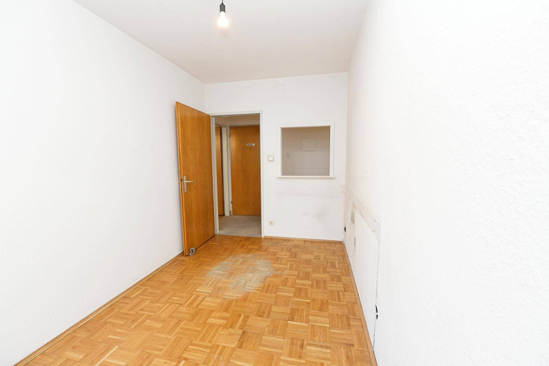 Kleiner Raum mit Fischgrätparkettboden und Holztür, ideal als Kinder- oder Gästezimmer.