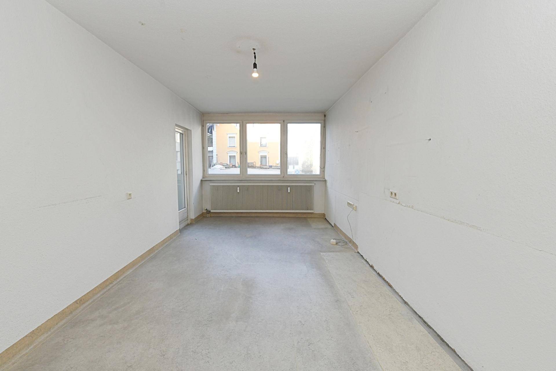 Geräumiges, unmöbliertes Zimmer mit großen Fenstern und Betonboden, bereit für die Gestaltung.