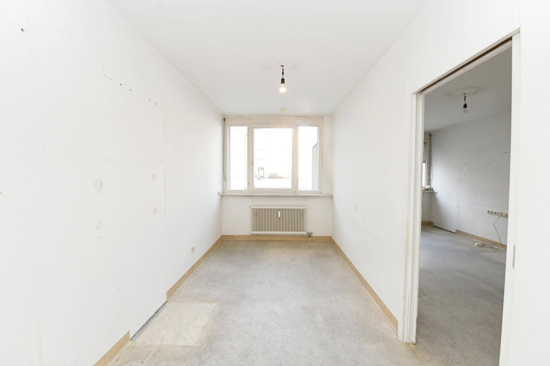 Kleiner, heller Raum mit Betonboden und Fenster, geeignet als Schlafzimmer oder Büro.