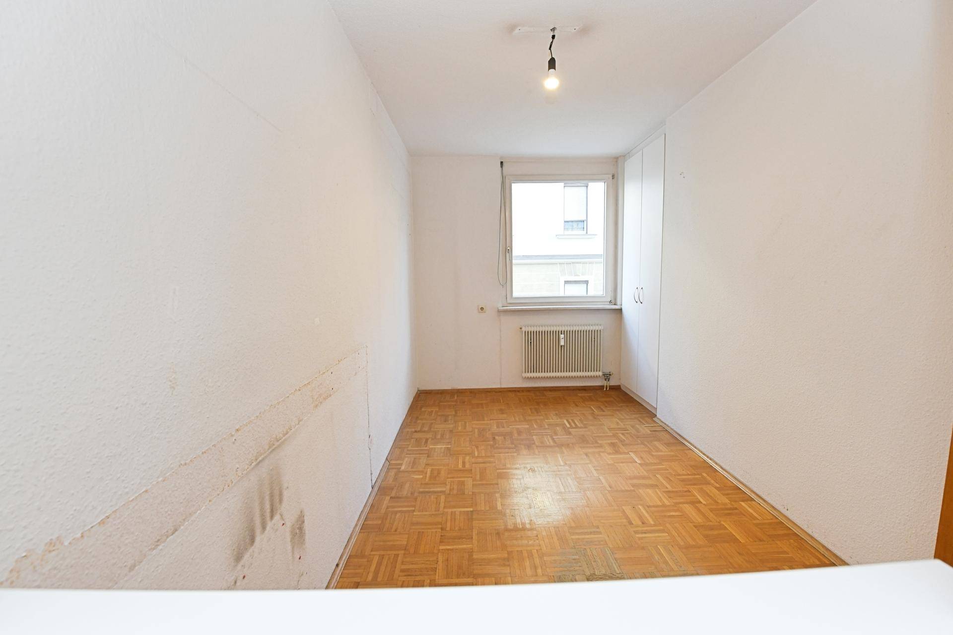 Helles Schlafzimmer mit Fischgrätparkettboden, Fenster und integriertem Kleiderschrank.