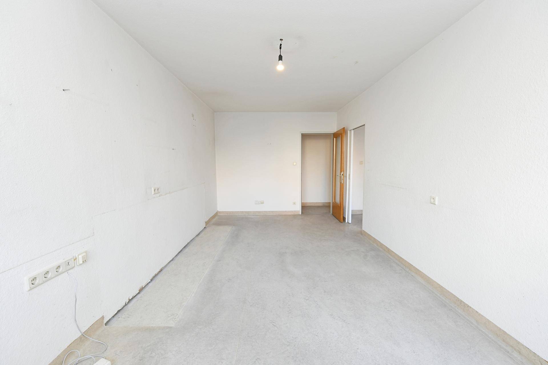 Unmöblierter Raum mit Betonboden und Zugang zu weiteren Zimmern, bietet viel Gestaltungspotenzial.
