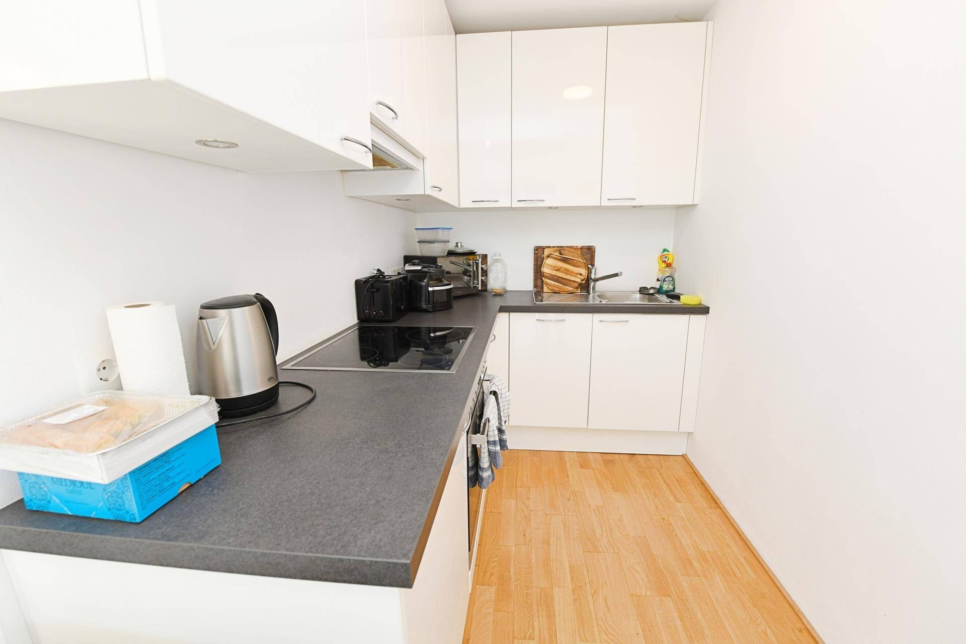 Moderne Einbauküche mit weißen Hochglanzschränken und dunkler Arbeitsplatte.