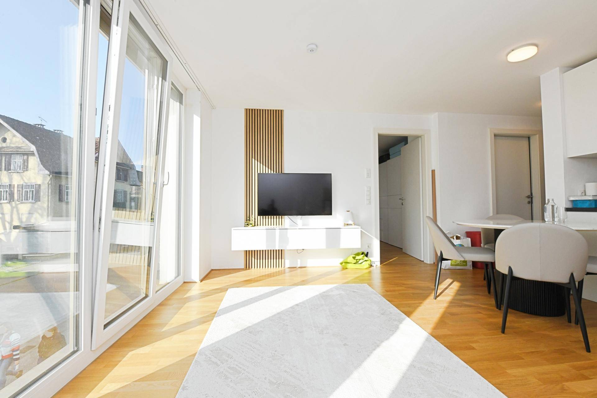 Heller Wohnbereich mit großem Fenster, Holzboden und modernem TV-Möbel.