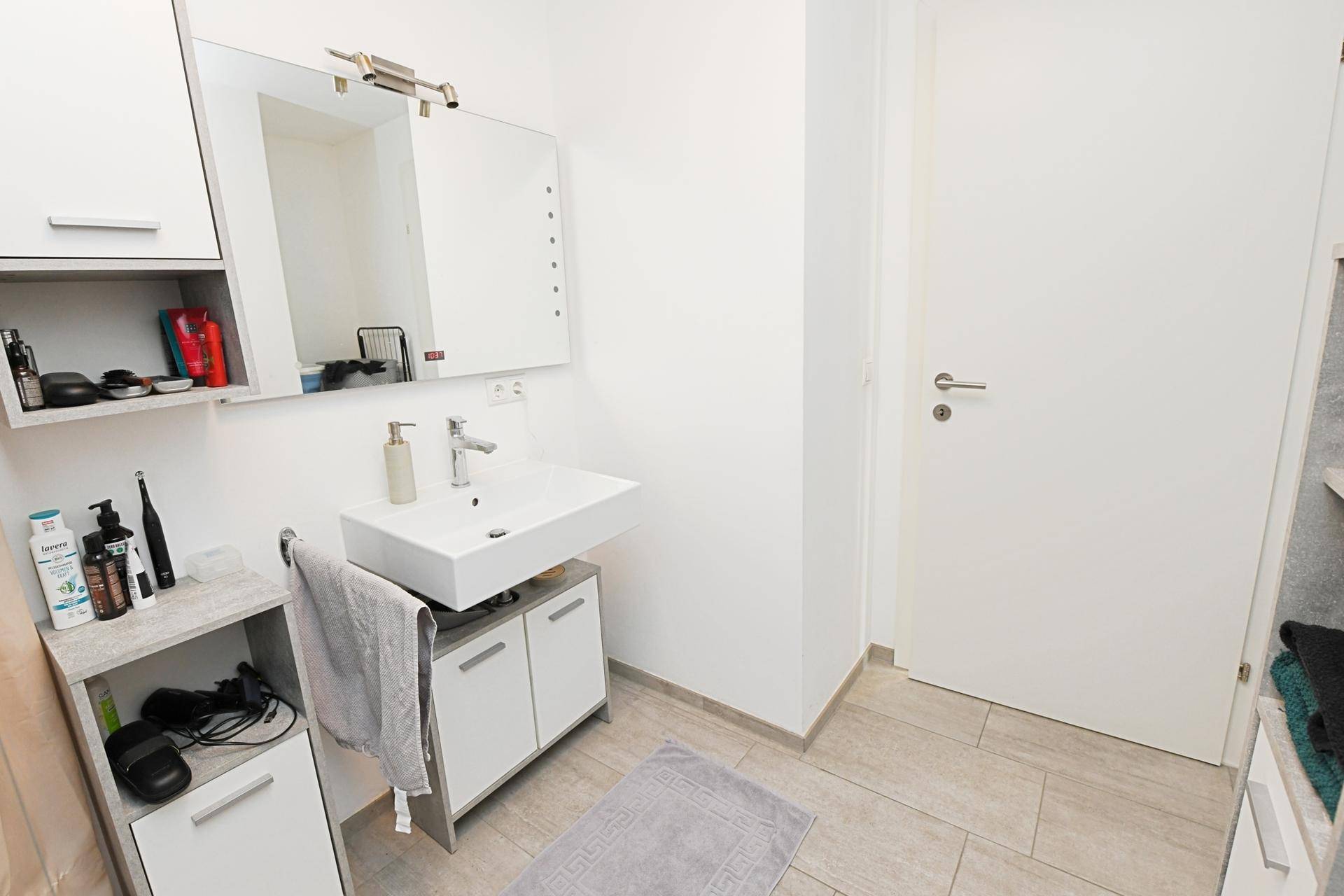 Modernes Badezimmer mit Waschbecken, Spiegelschrank und hellen Fliesen.