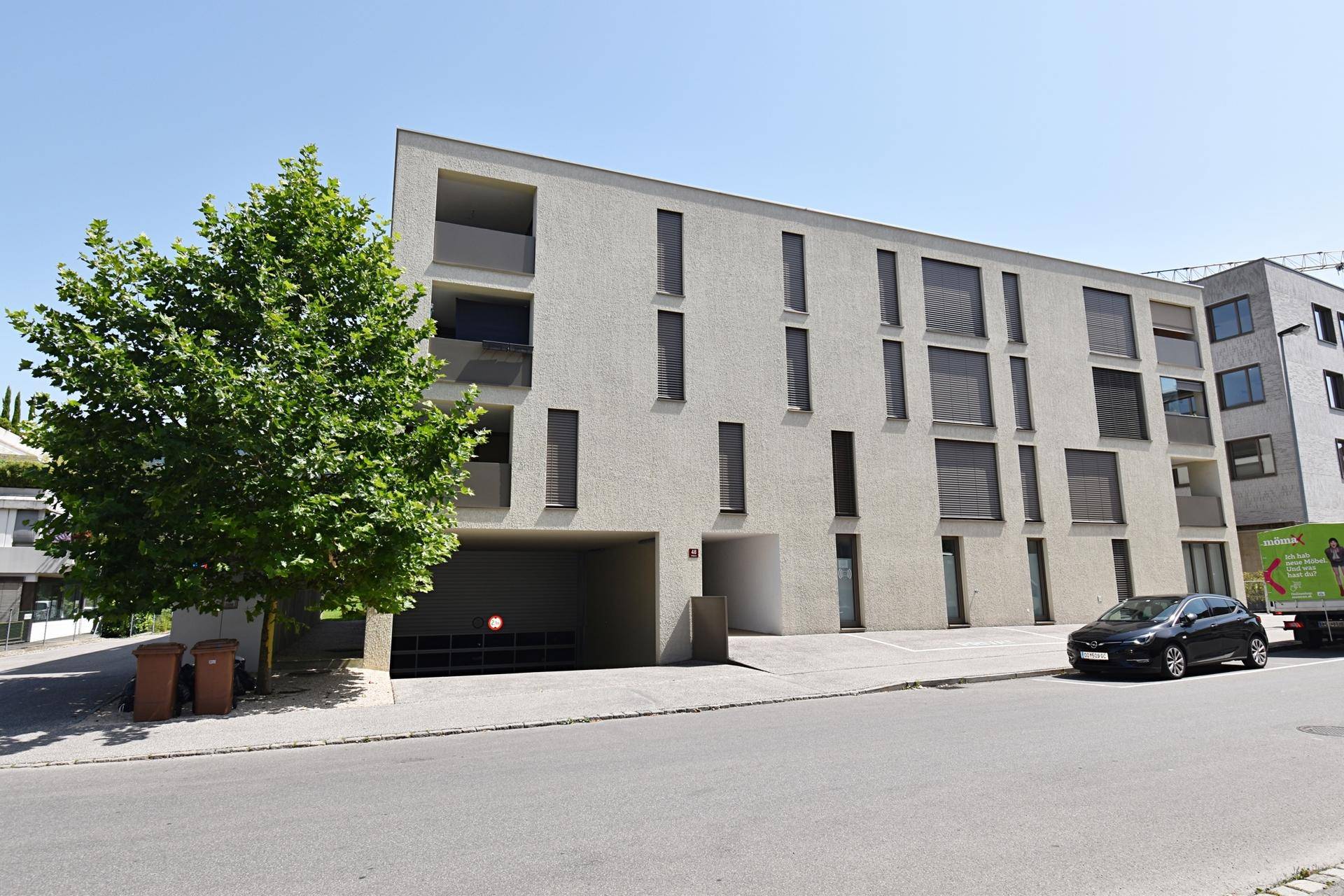 Modernes Wohngebäude mit Tiefgaragenzufahrt und Bäumen an der Straßenseite.